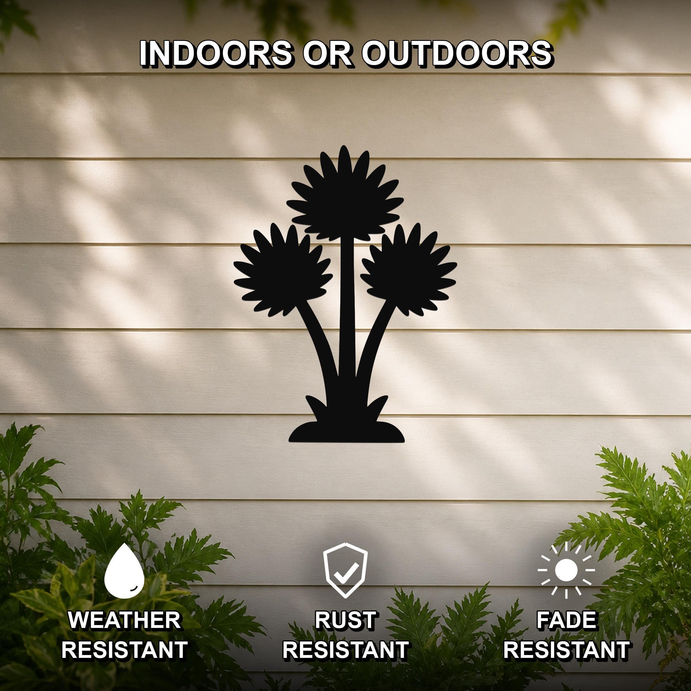 Black metal wall art featuring a silhouette of three wildflowers, mounted on a beige outdoor wall with greenery below, weather resistant, rust resistant, and fade resistant.