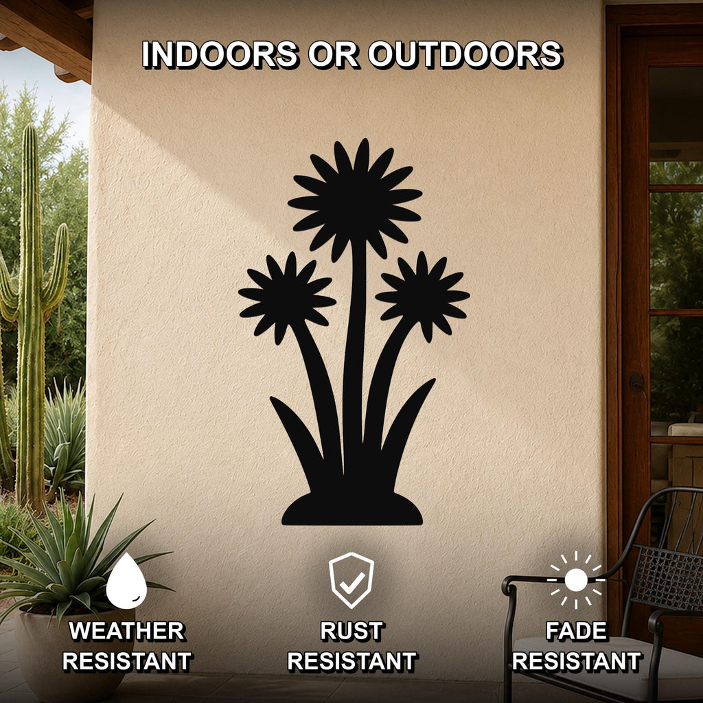 Black metal wall art featuring a silhouette of three wildflowers with layered petals and long stems, mounted on an outdoor patio wall beside a potted succulent and a cactus.