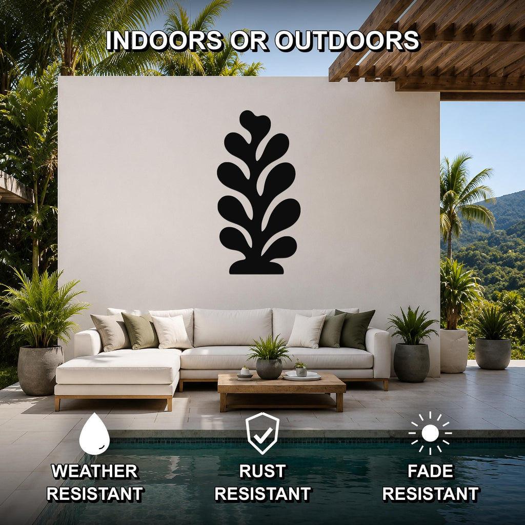 Black metal coral wall art with leafy cutout design, mounted on a white outdoor wall above a sofa in a patio living area.