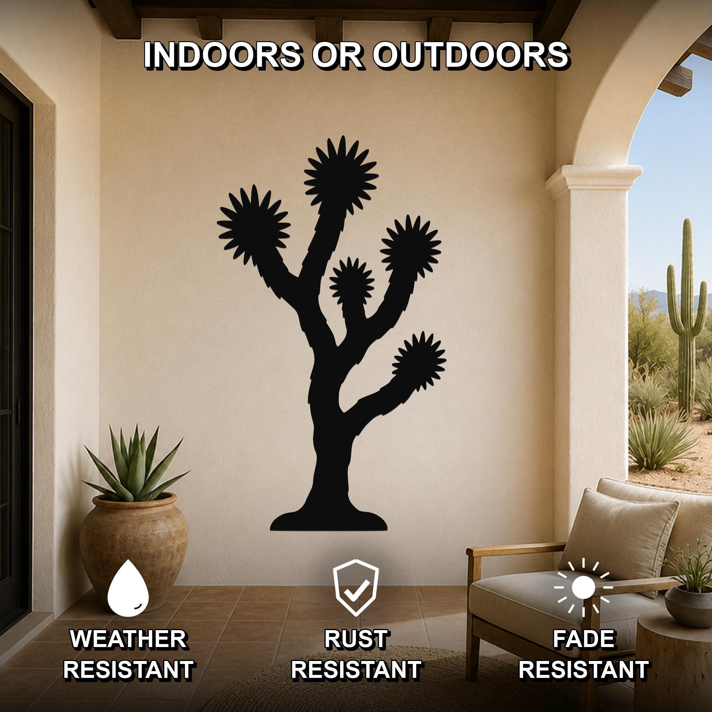 Black metal Joshua tree wall art silhouette with branch and flower cutouts, mounted on a beige patio wall above a chair and potted plant.