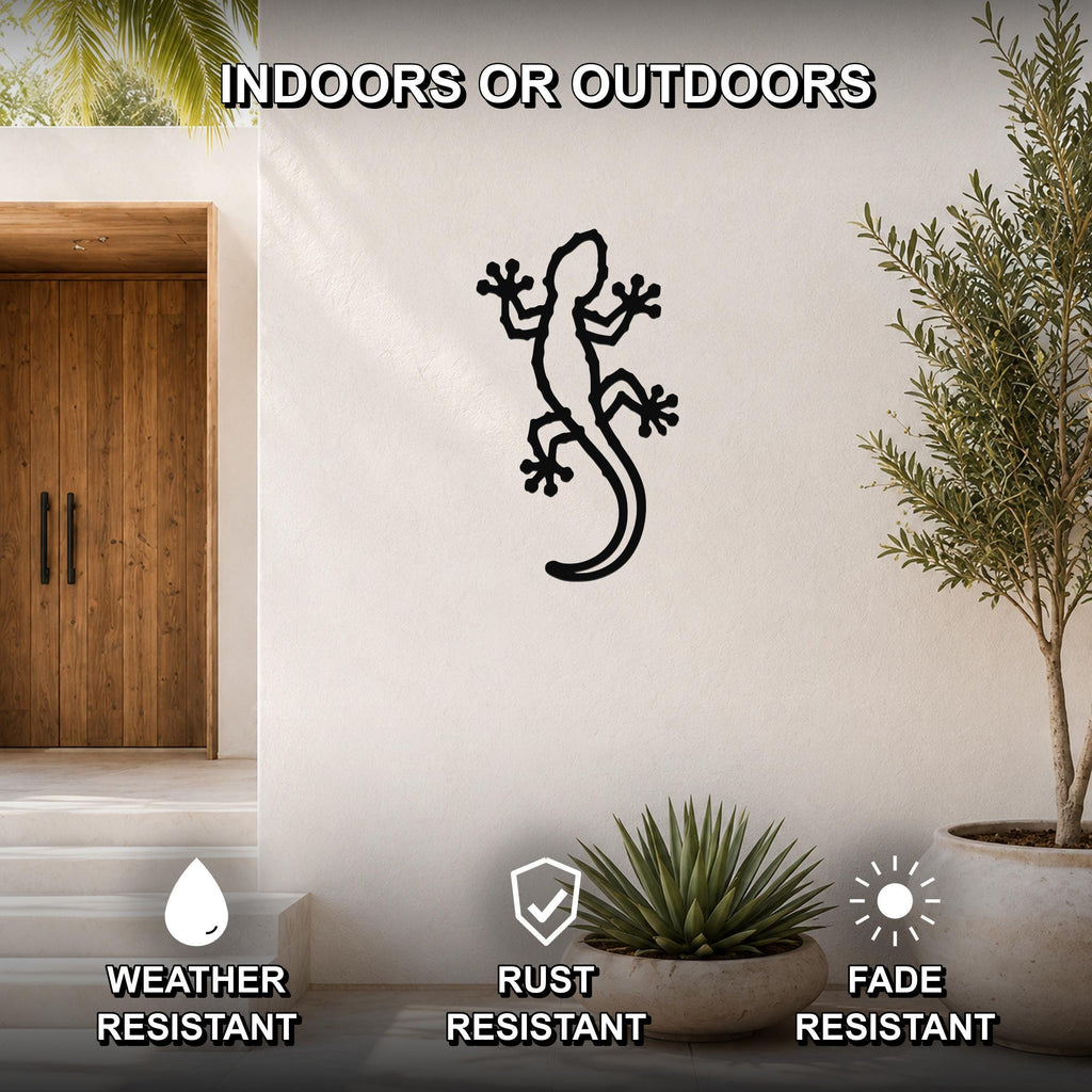 Black metal gecko wall art with detailed cutout limbs and tail, mounted on a white outdoor wall beside a wooden door and potted plants.