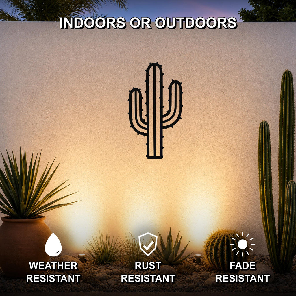 Black metal saguaro cactus wall art with spines and arms, mounted on an outdoor wall above a desert garden with potted plants and pebbles.