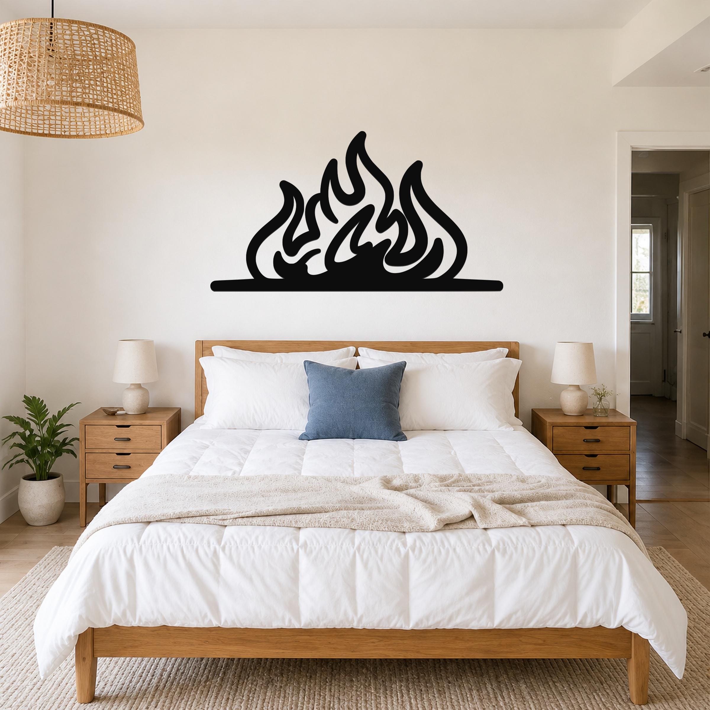 Black metal flame silhouette wall art with fluid, layered cutouts, mounted above a wooden bed in a neutral bedroom.