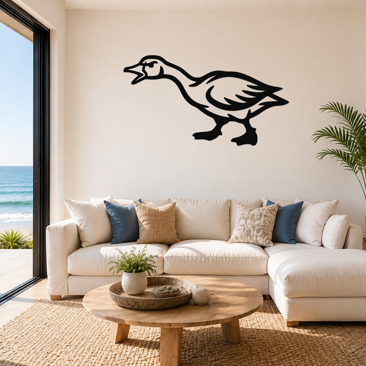 Black metal goose wall art with a bold silhouette design, mounted above a white sofa in a bright living room with ocean views.