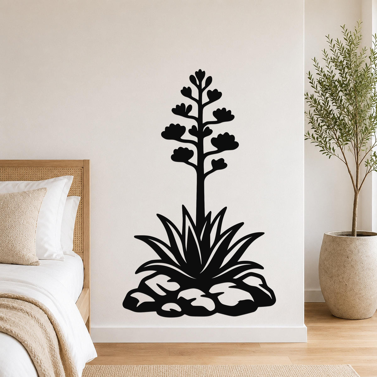 Black metal agave wall sculpture with blooming flower and spiky leaves, mounted on a bedroom wall above a bed.