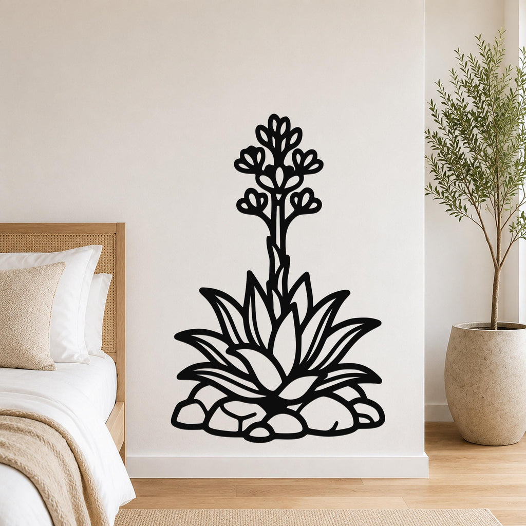 Black metal agave wall art with blooming flower and leaf cutouts, mounted on a bedroom wall above a bed.