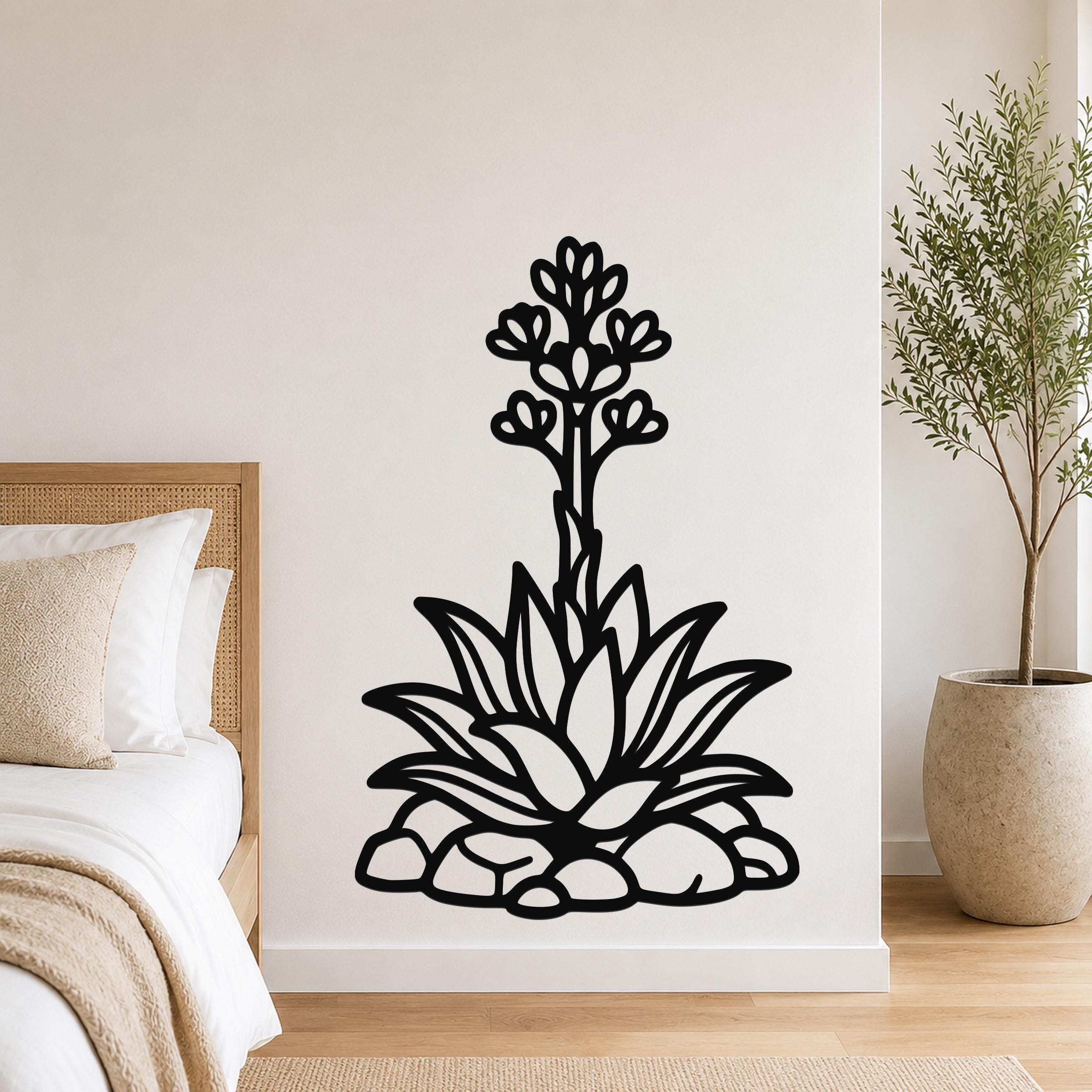 Black metal agave wall art with blooming flower and leaf cutouts, mounted on a bedroom wall above a bed.