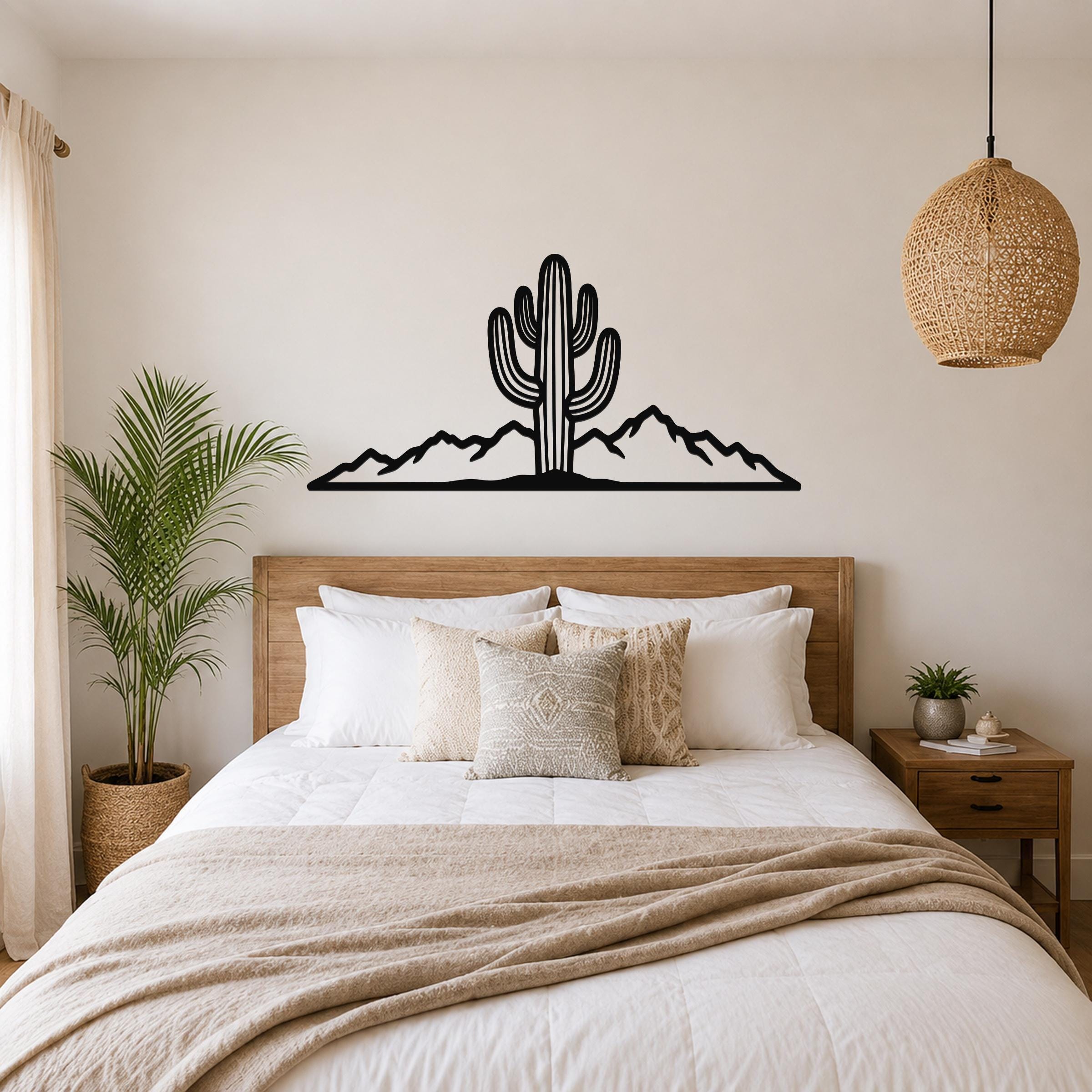 Black metal wall art silhouette of a saguaro cactus and mountain range, mounted above a wooden bed in a bedroom.