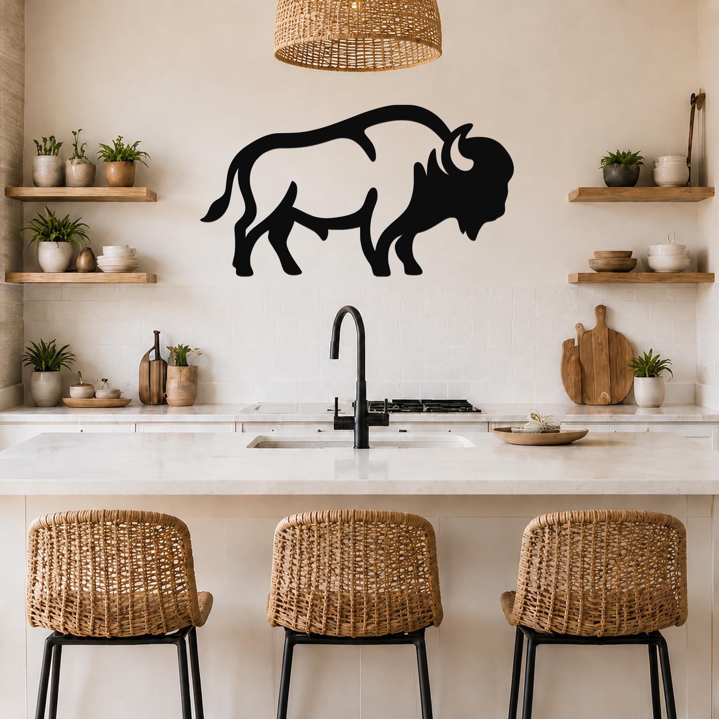 Black metal bison silhouette wall art mounted on a kitchen wall above a counter, with visible horns and tail, in a rustic modern kitchen with wicker chairs and open shelves.