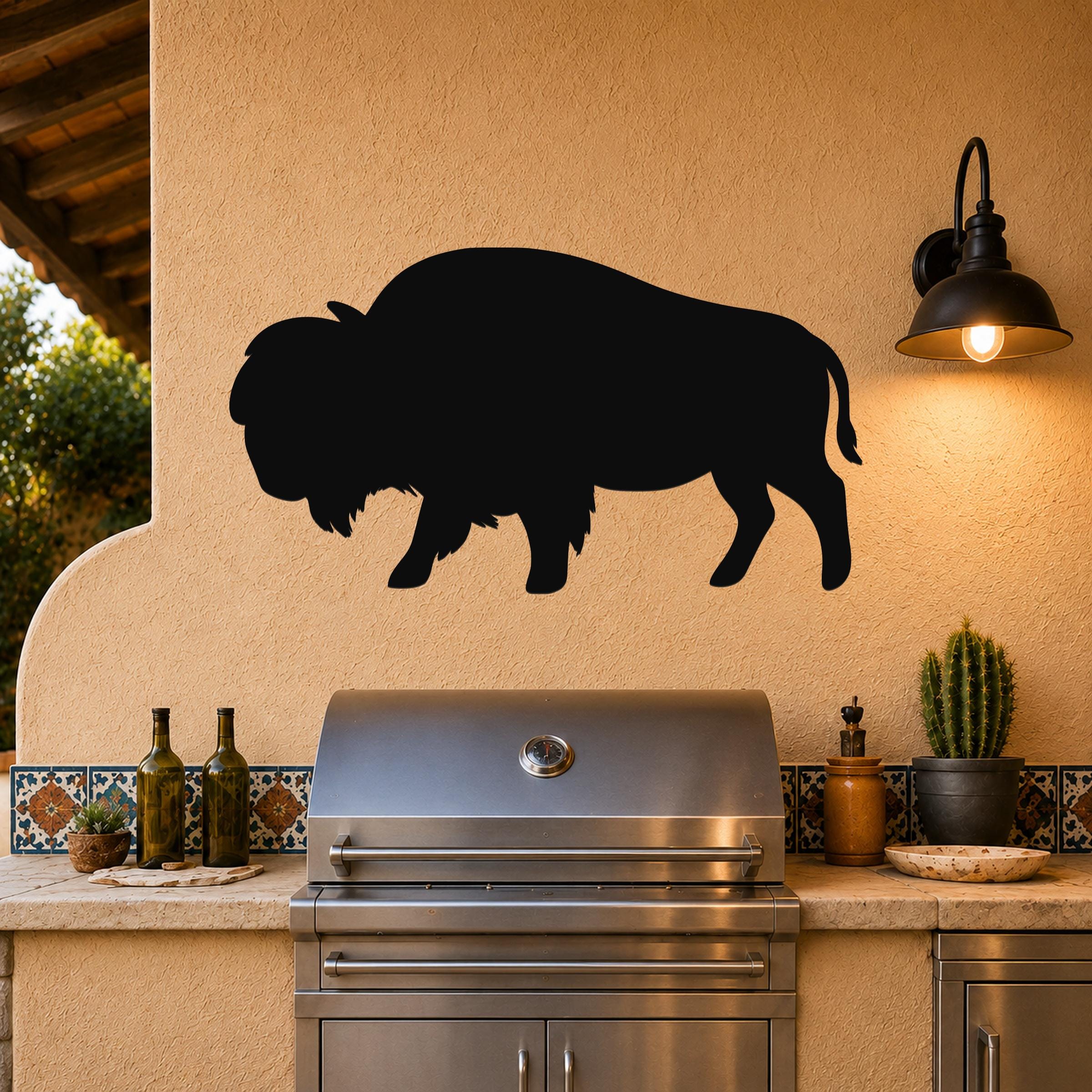 Black metal bison silhouette wall art mounted on a stucco wall above a stainless steel grill in an outdoor kitchen.
