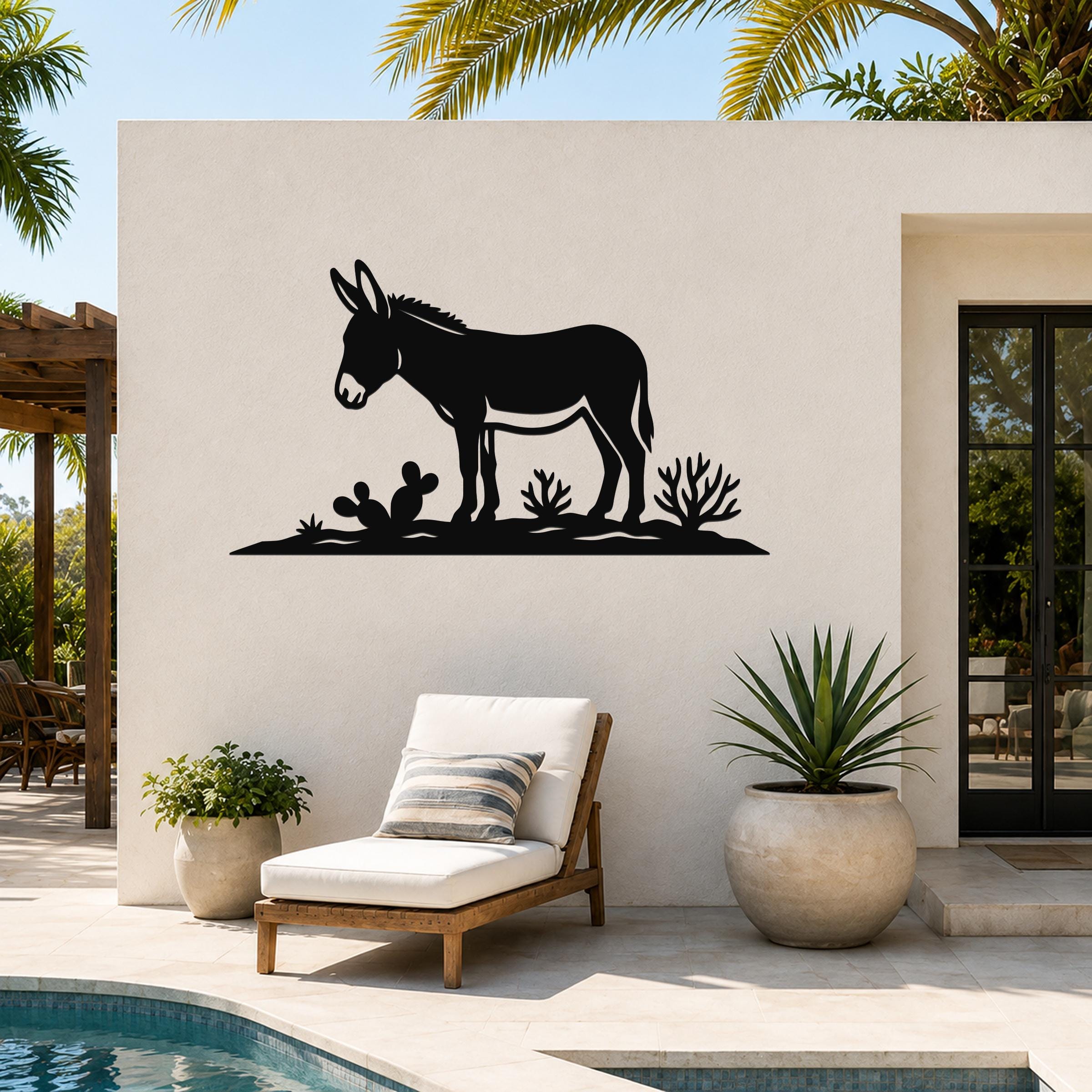 Black metal wall art silhouette of a burro with cacti, mounted on an outdoor patio wall near a pool and lounge chair.