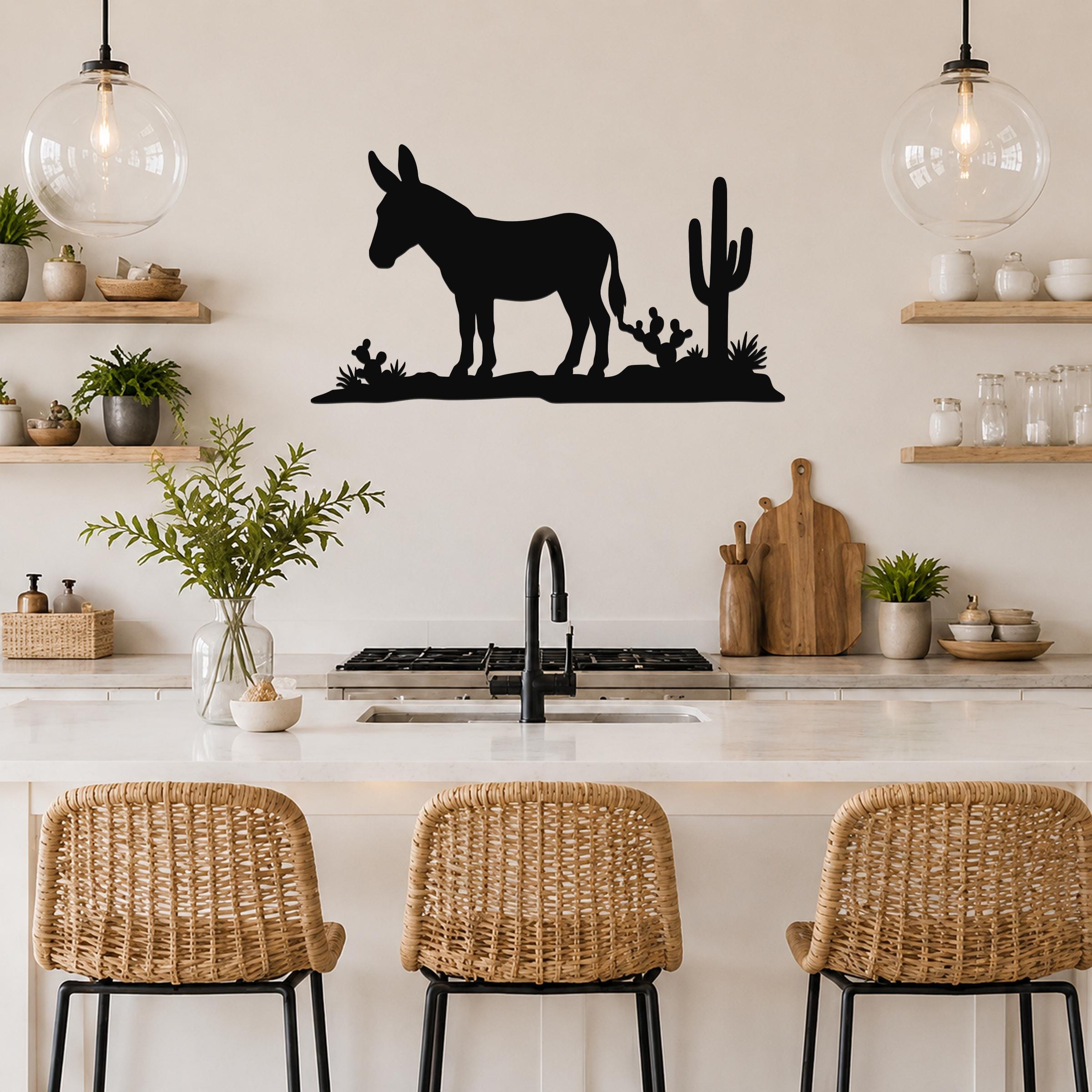 Black metal wall art silhouette of a burro and cacti, mounted above a kitchen counter with pendant lights and wicker stools.