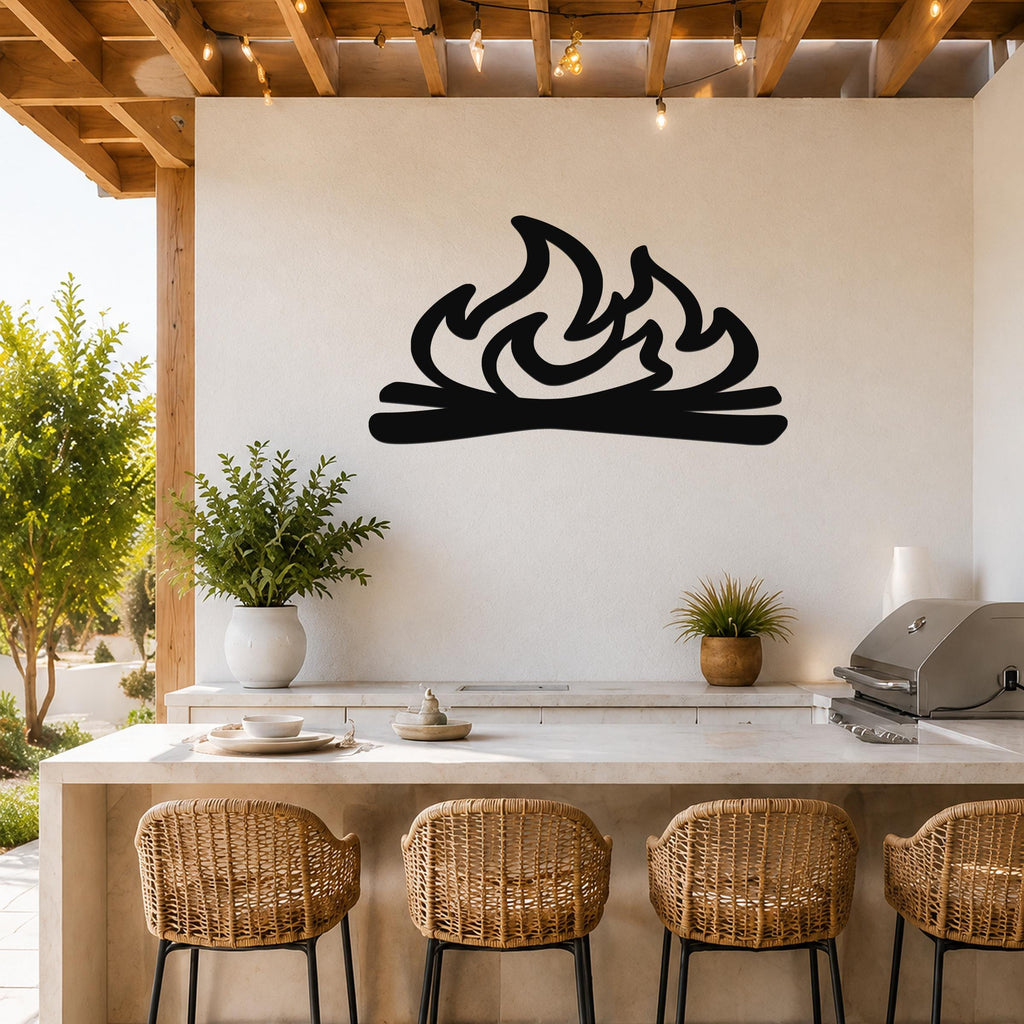 Black metal campfire wall art with flame and log silhouette, mounted on a white outdoor wall above a kitchen counter.