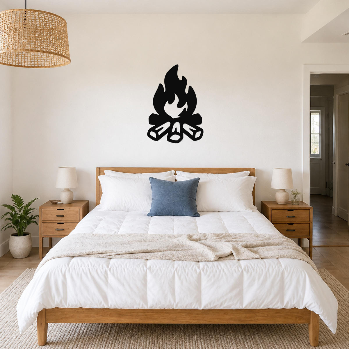 Black metal campfire wall art with flame and log silhouette, mounted above a bed in a bedroom.
