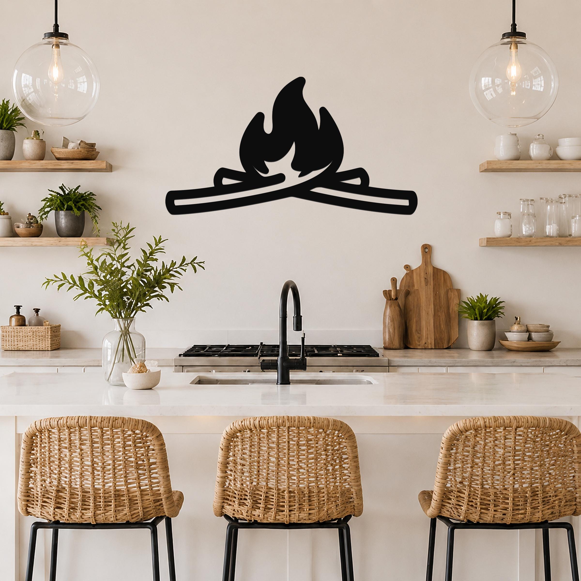 Black metal campfire wall art with flame and log silhouette, mounted on a kitchen wall above a counter with wicker bar stools.