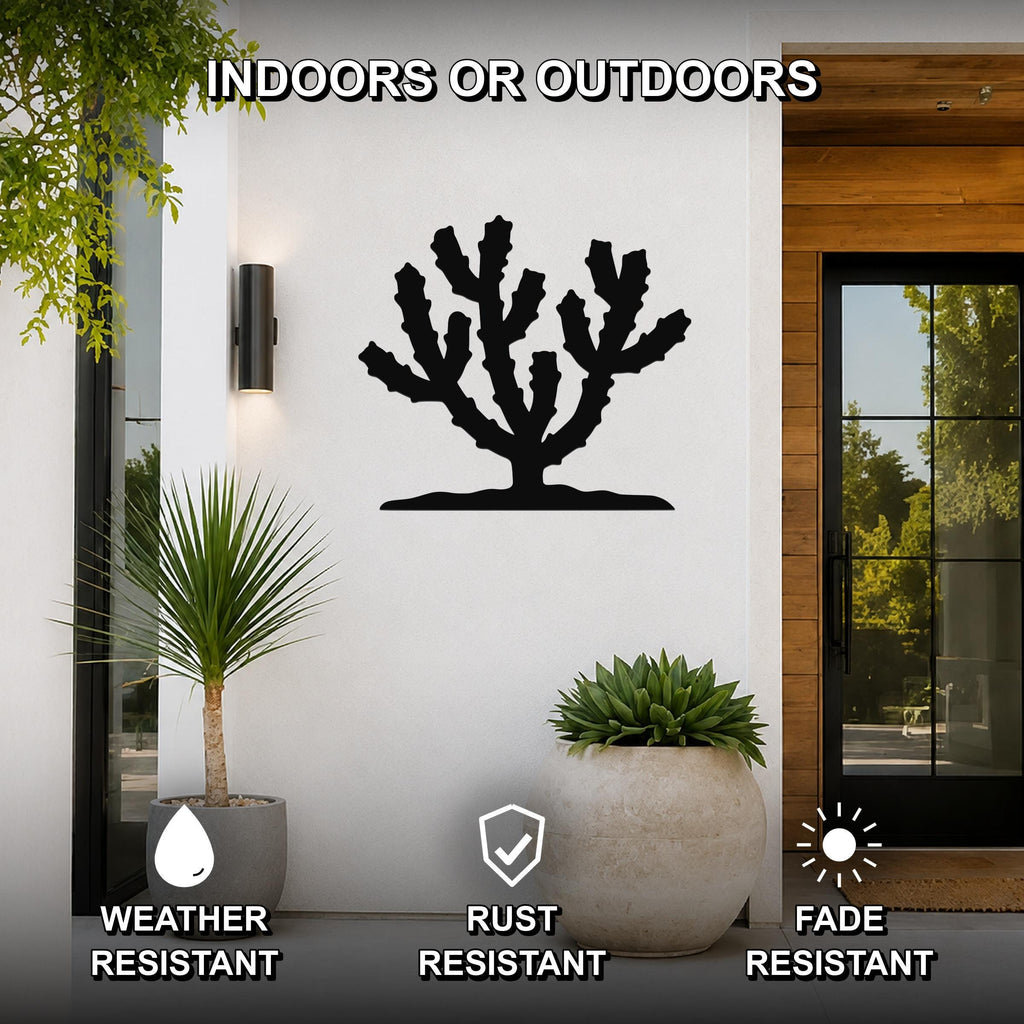 Black metal cholla cactus wall art silhouette mounted on a white exterior wall beside a glass door and potted plants, with text indicating it is weather, rust, and fade resistant.