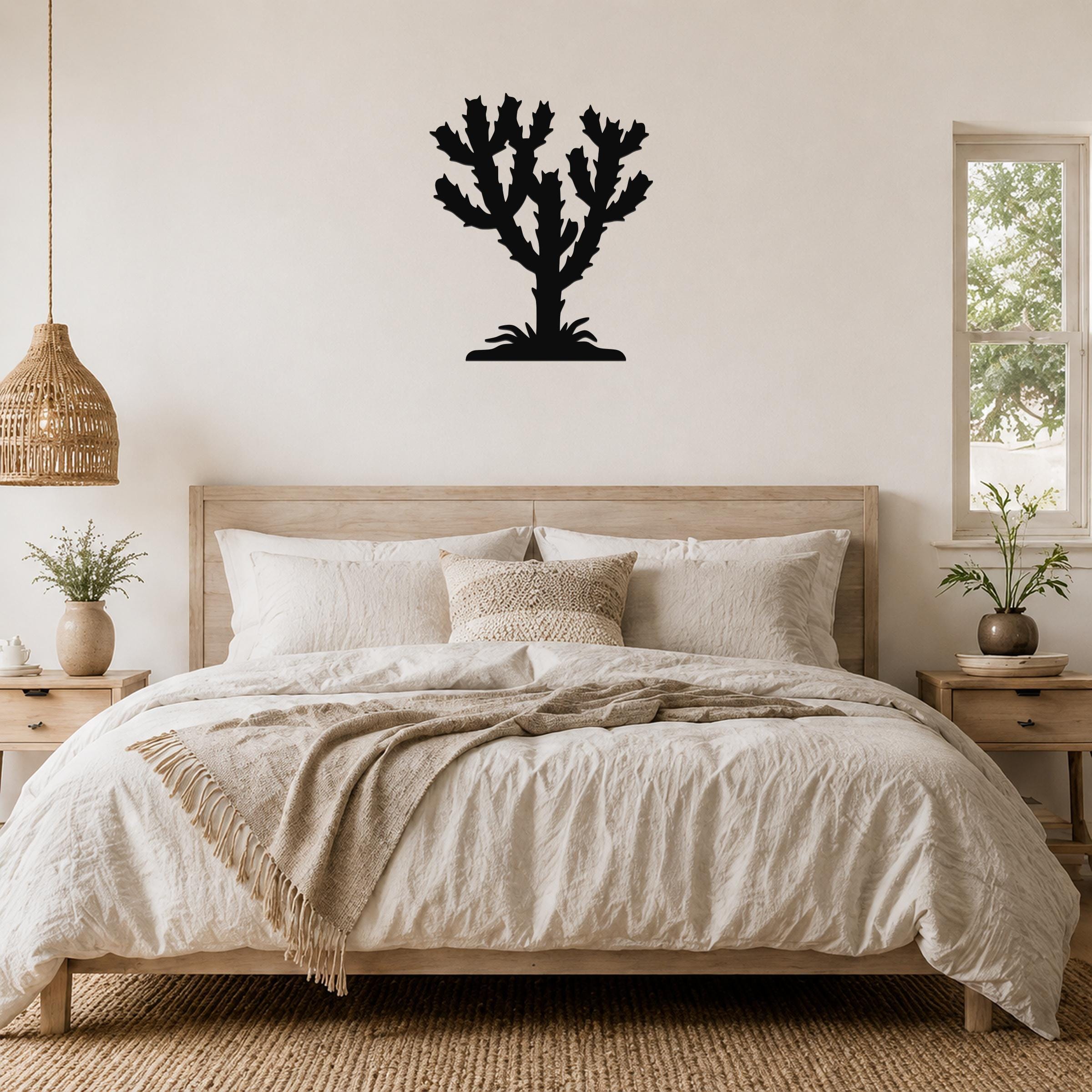Black metal Cholla cactus wall art silhouette mounted above a wooden bed in a neutral bedroom.