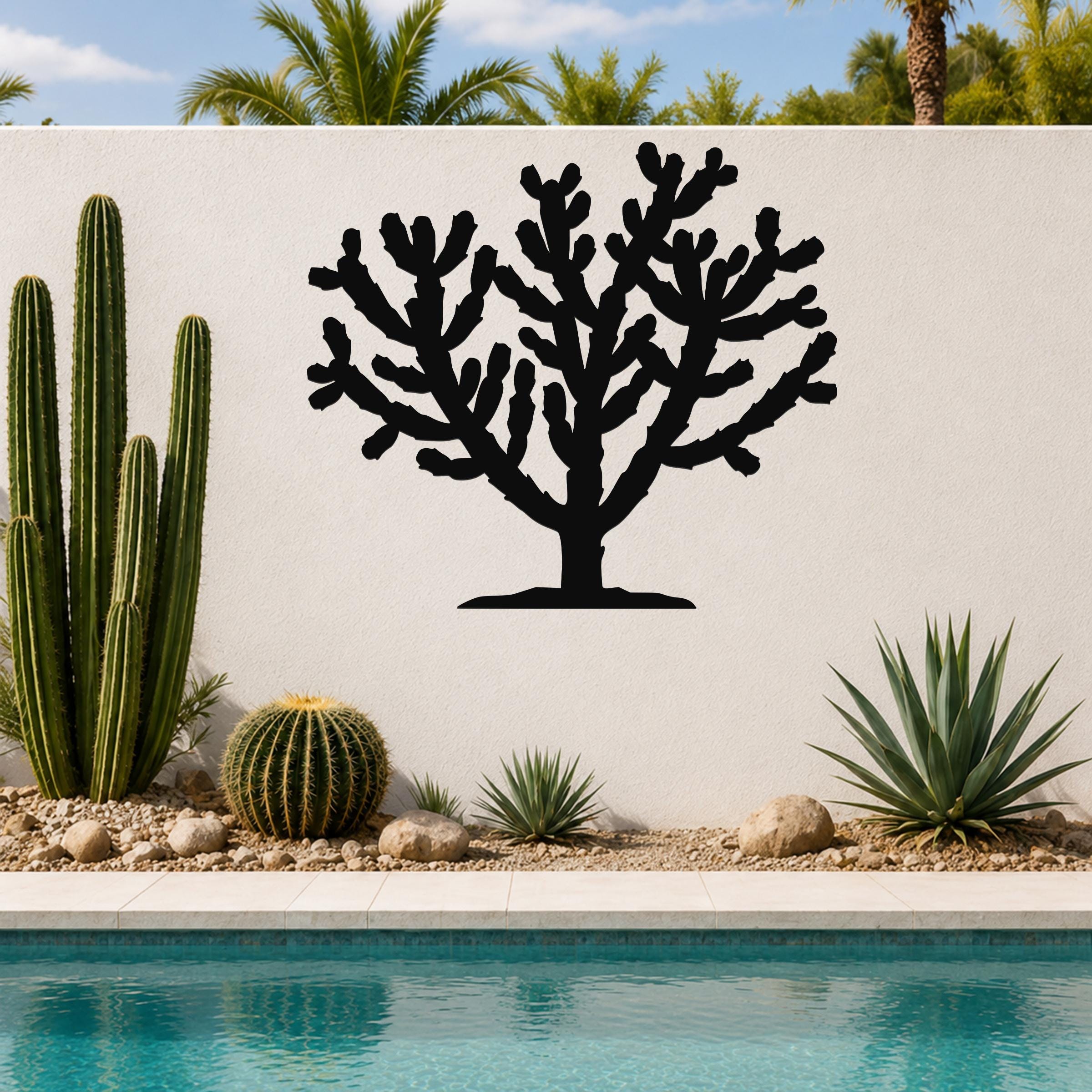 Black metal Cholla cactus wall art silhouette with branching arms, mounted on a white outdoor wall above a poolside garden.