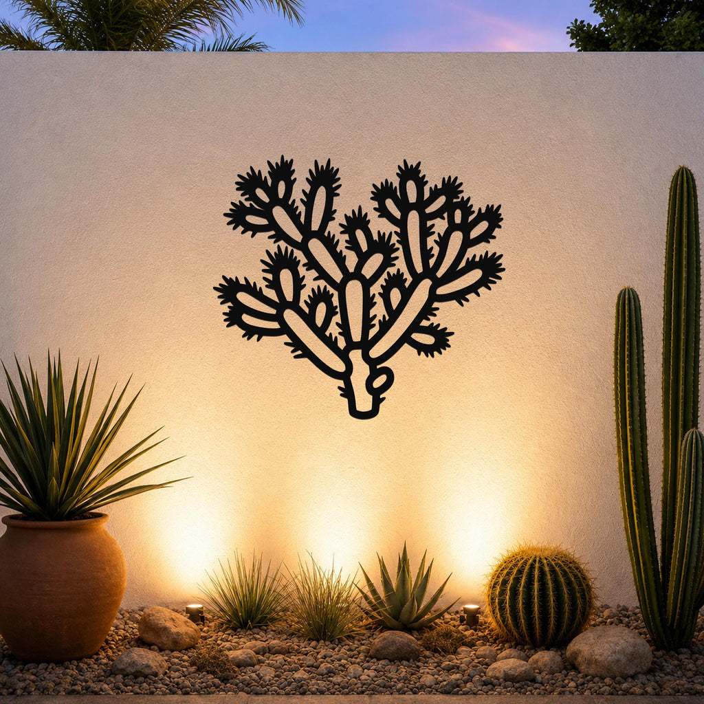 Black metal cholla cactus wall art with detailed branch and spine cutouts, mounted on a light-colored outdoor wall above a desert garden with potted plants and ground lights.