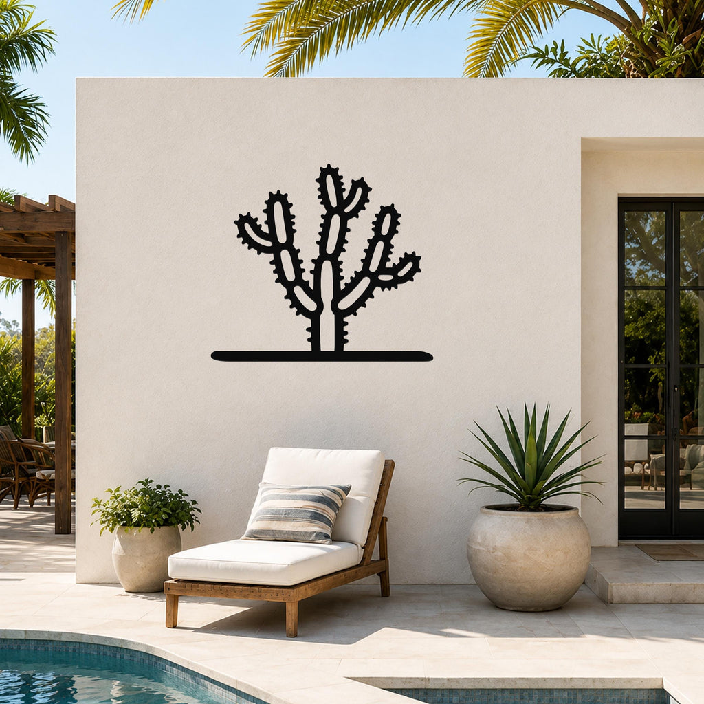 Black metal Cholla cactus wall art with spiny branch cutouts, mounted on a white outdoor wall beside a poolside lounge chair.