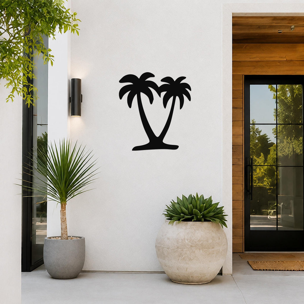 Black metal palm tree wall art with two silhouetted trees, mounted on a white exterior wall beside a glass door and potted plants.