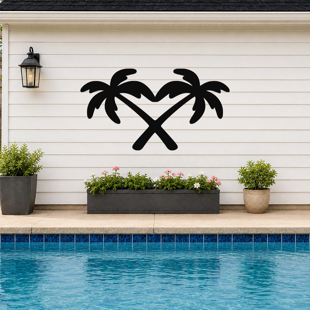 Black metal wall art featuring two crossed palm tree silhouettes, mounted on a white horizontal siding wall above a poolside planter.