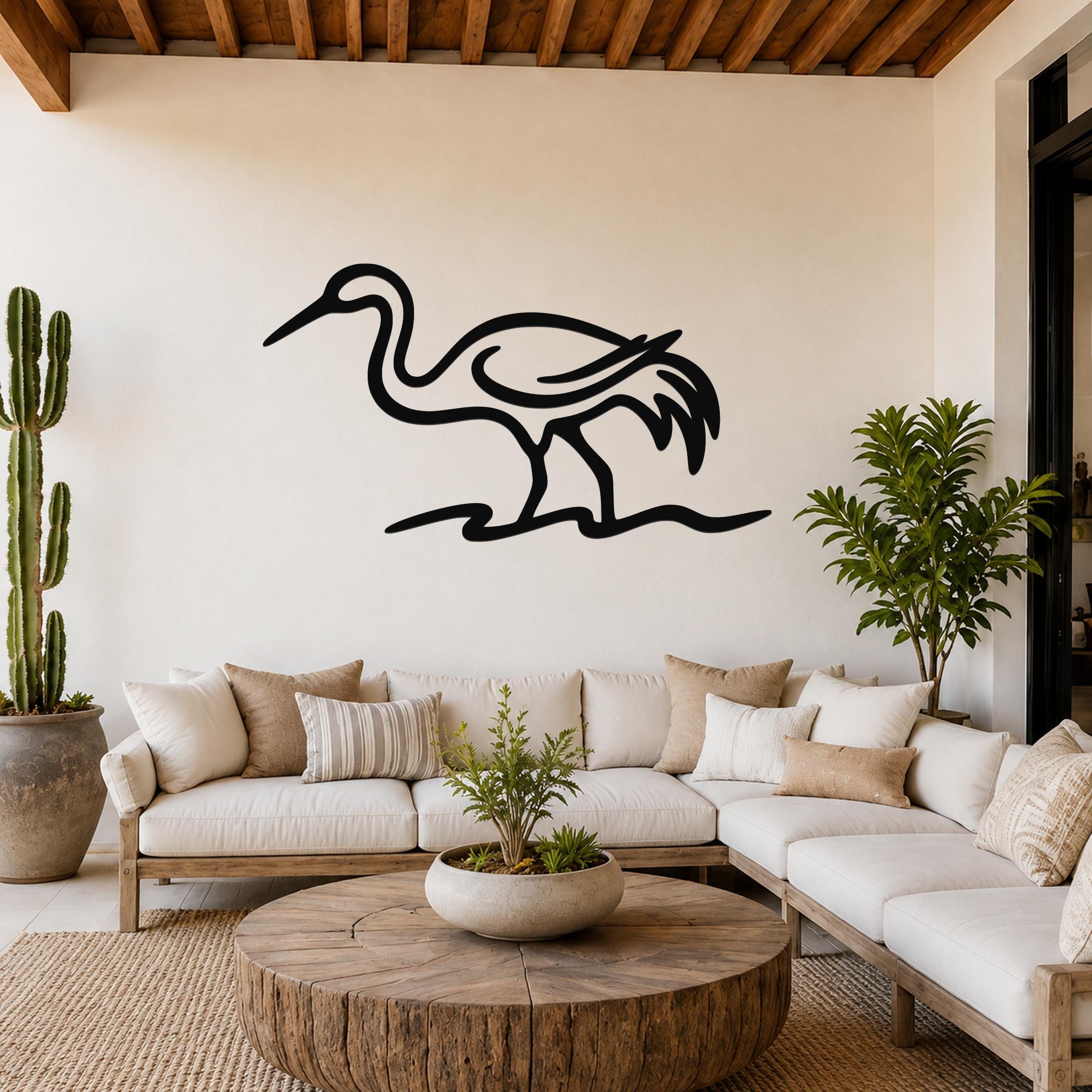 Black metal crane wall art with flowing line cutouts, mounted above a white sofa in a living room.