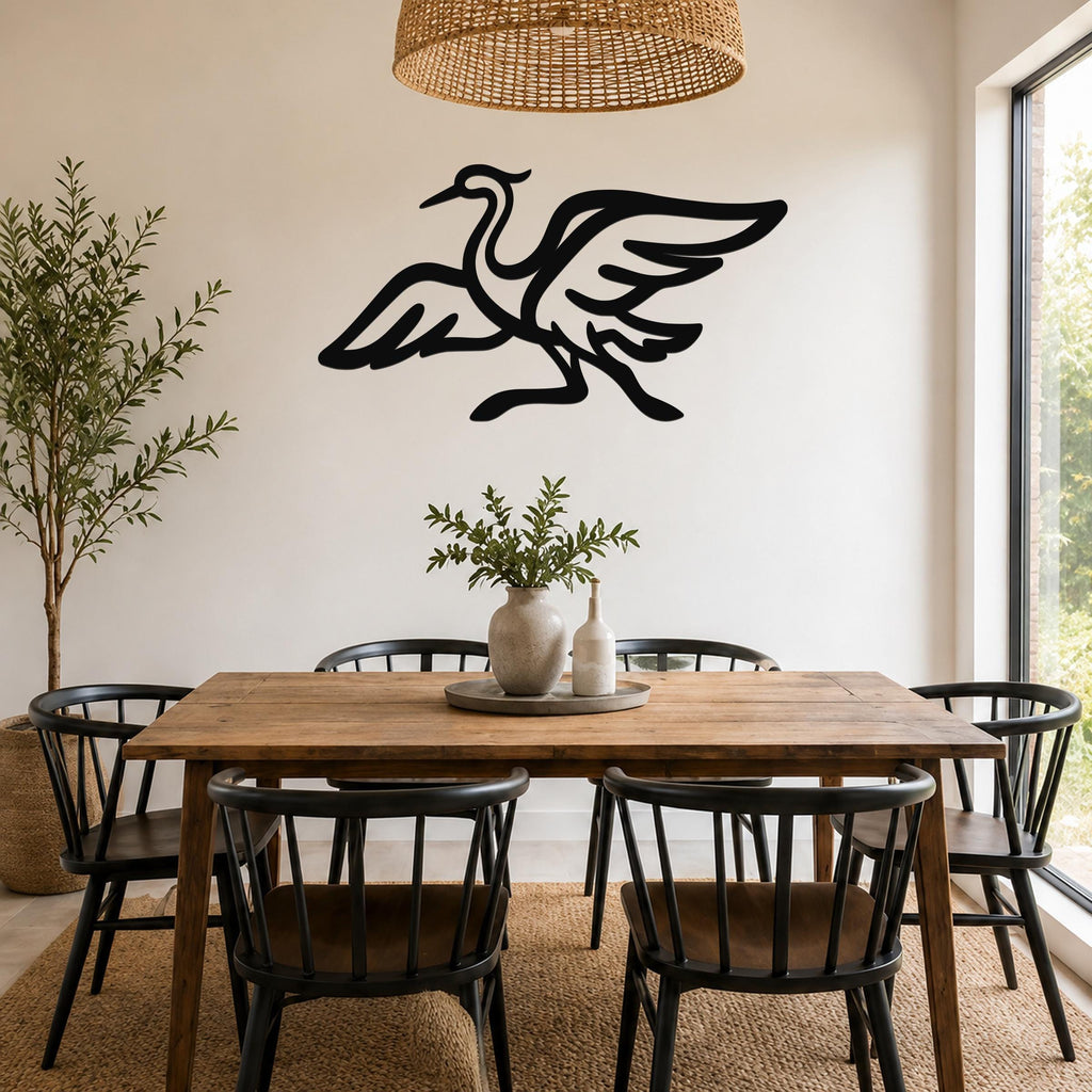 Black metal crane wall art with outstretched wings and detailed feather cutouts, mounted on a white wall above a wooden dining table in a bright dining room.