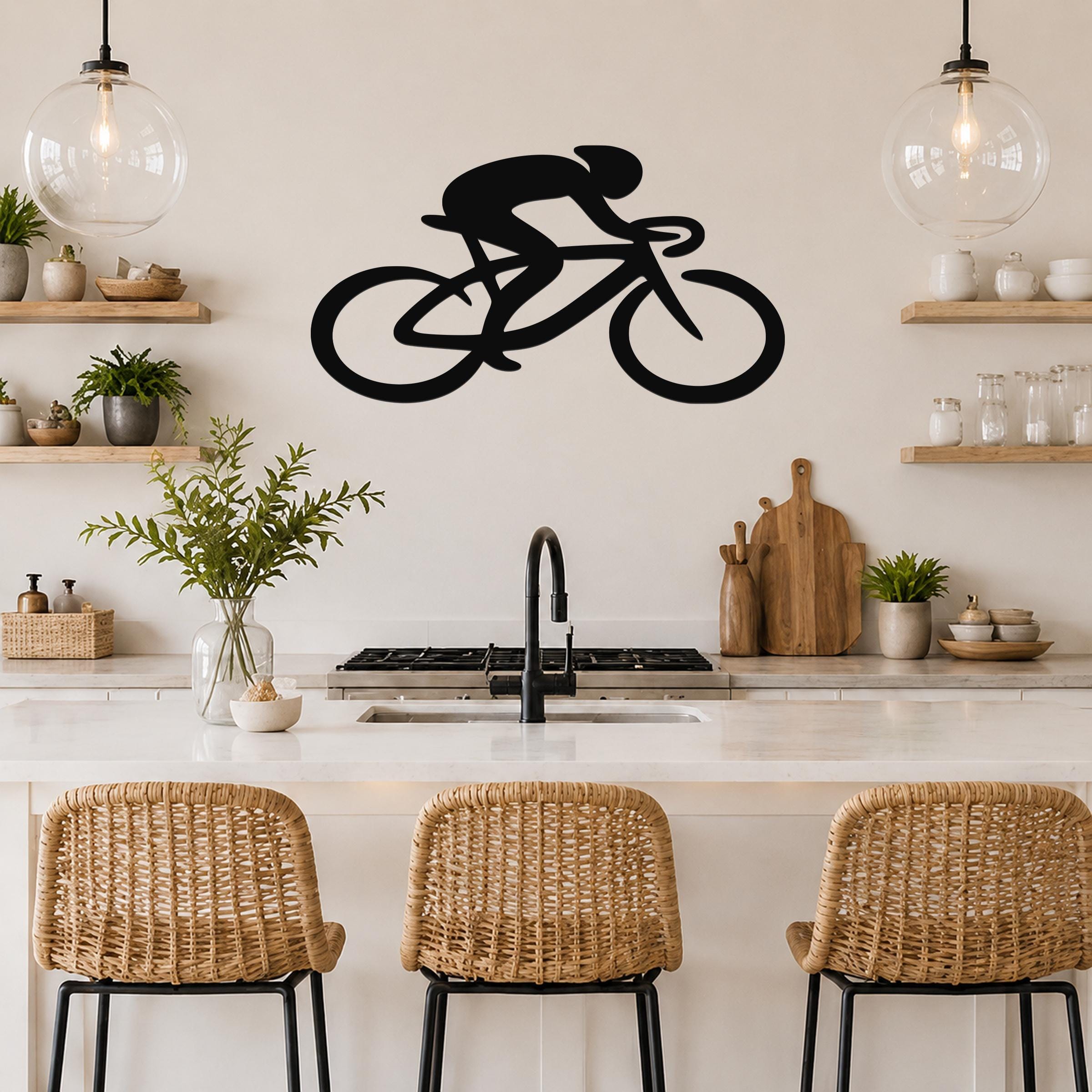 Black metal wall art of a cyclist silhouette in motion, mounted above a kitchen counter with pendant lights and wooden shelves.