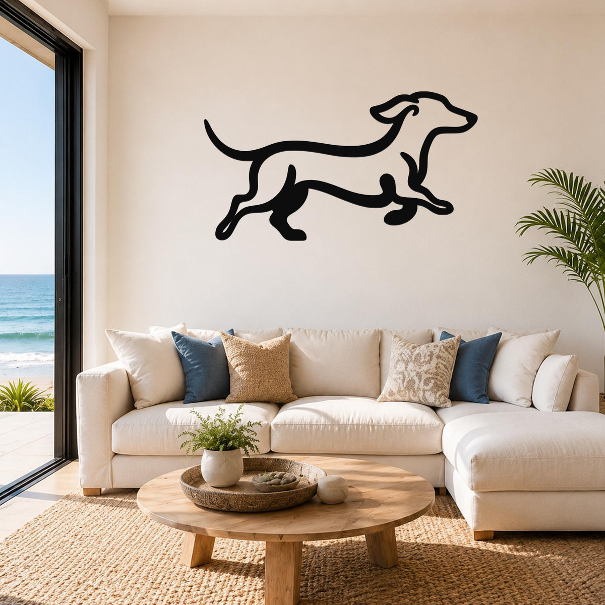 Black metal dachshund wall art in a running silhouette, mounted above a white sofa in a living room with ocean views.