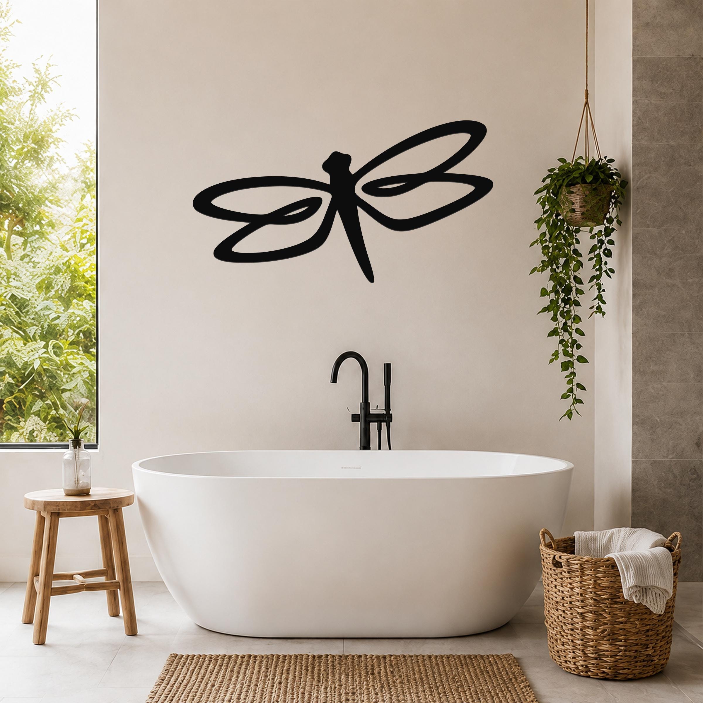 Black metal dragonfly wall art with flowing wing cutouts, mounted on a bathroom wall above a freestanding tub.