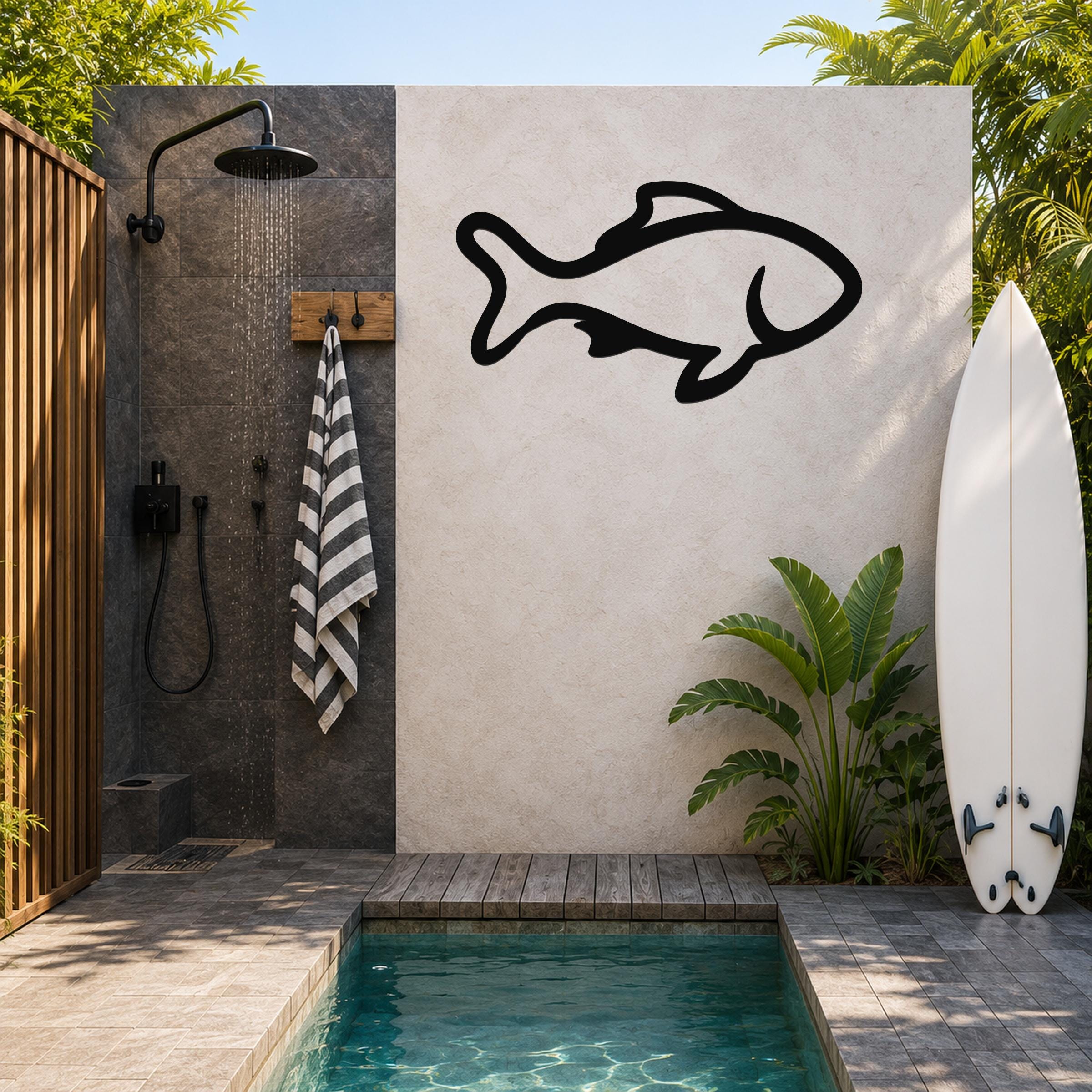 Black metal fish wall art with bold outline cutout, mounted on a light-colored outdoor wall beside a shower and pool area.