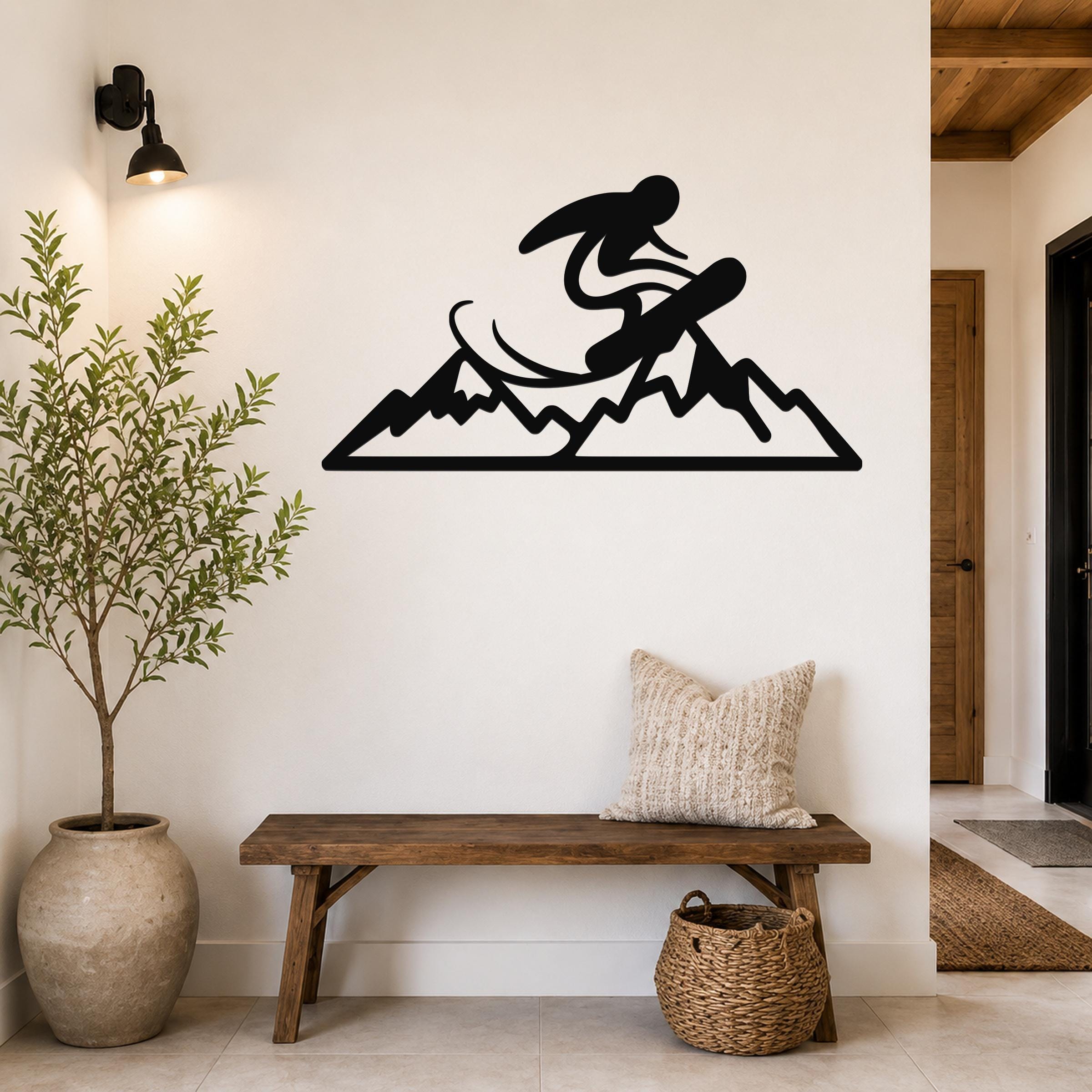 Black metal wall art featuring a snowboarder silhouette above mountain peaks, mounted on a white wall above a wooden bench in a hallway.