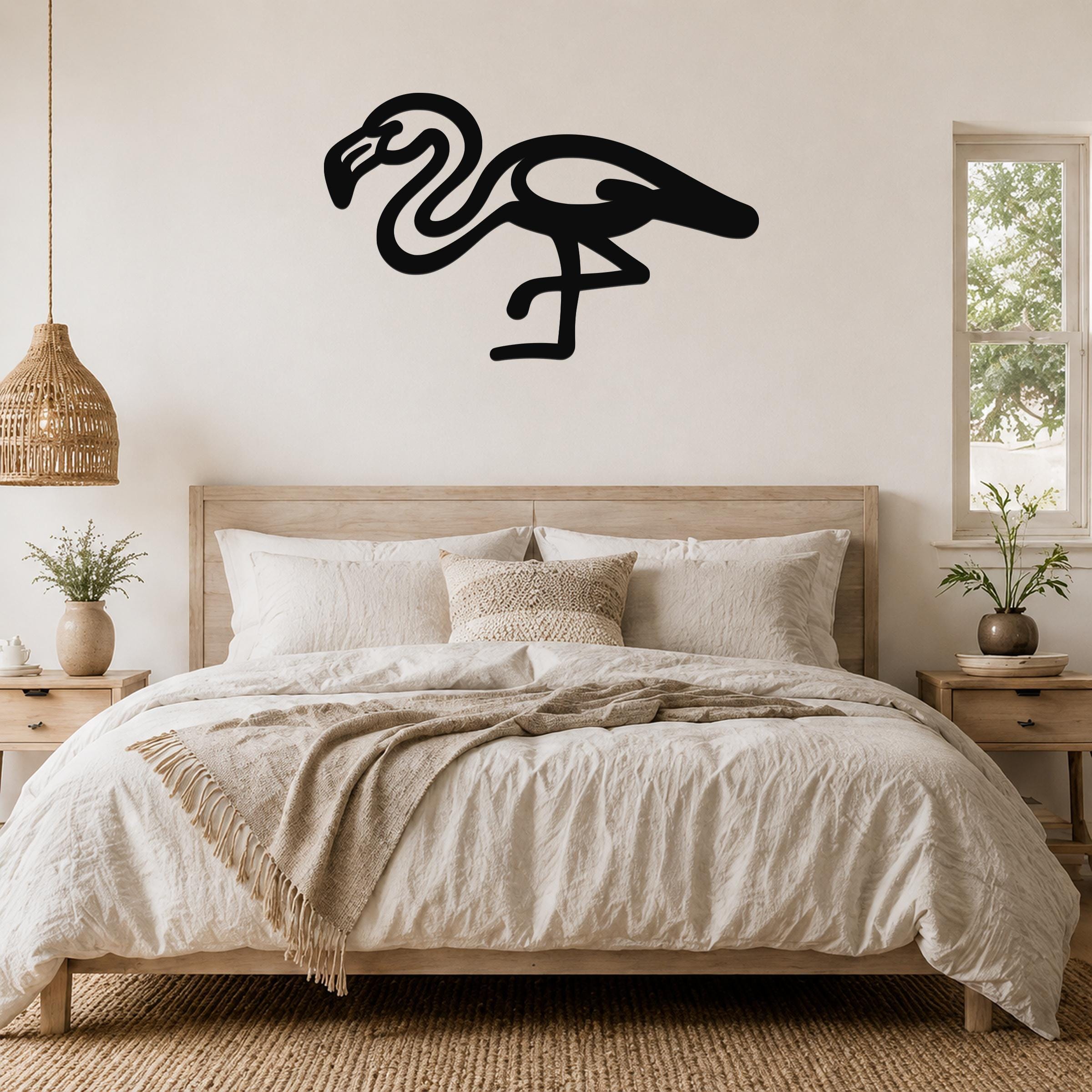 Black metal flamingo wall art with a minimalist silhouette design, mounted on a wall above a bed in a neutral bedroom.