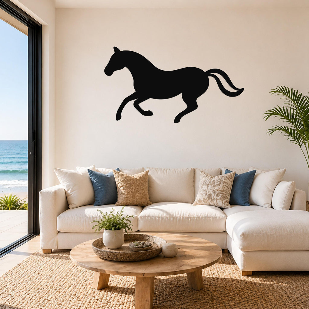 Black metal horse wall art silhouette in a running pose, mounted above a white sectional sofa in a living room with ocean views.
