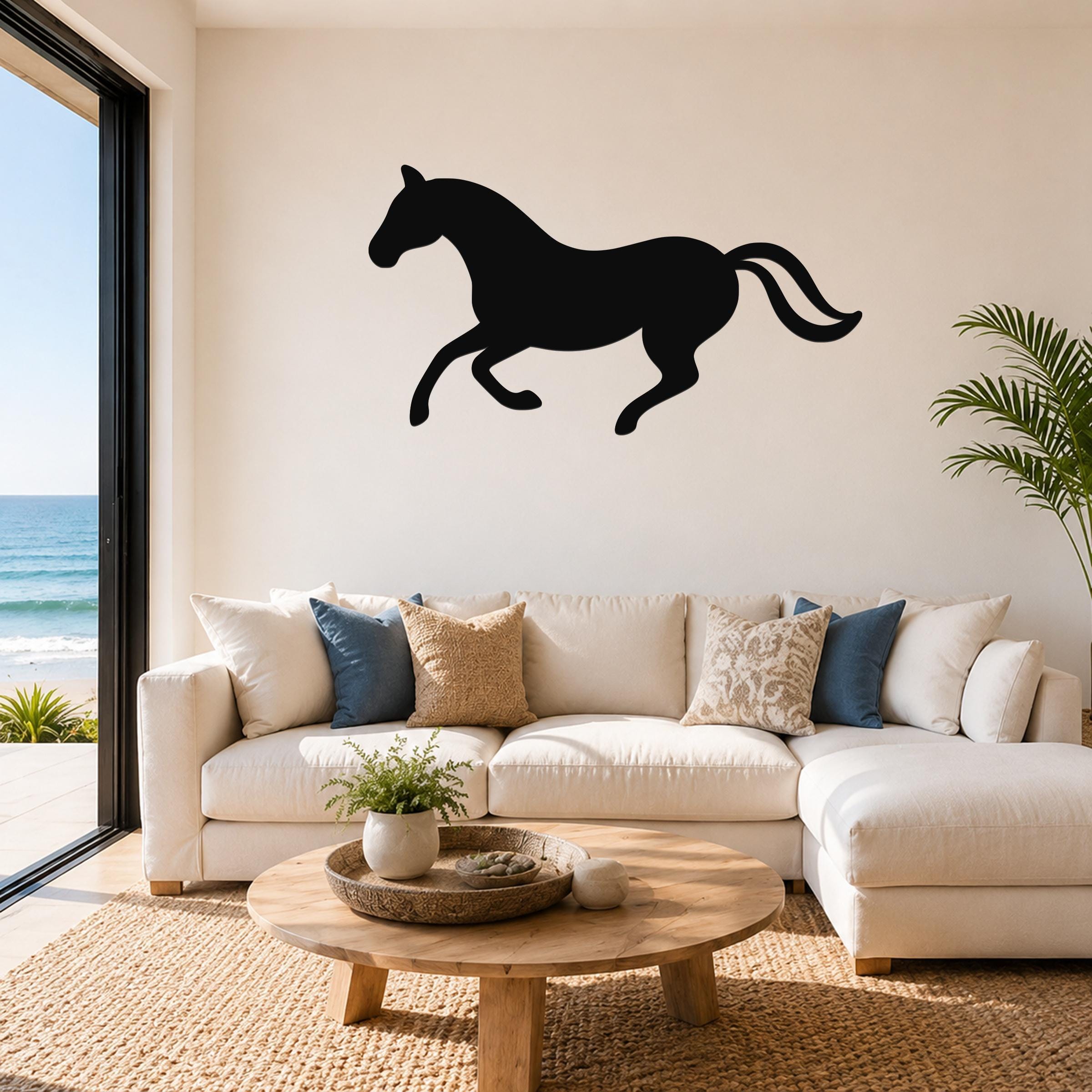 Black metal horse wall art silhouette in a running pose, mounted above a white sectional sofa in a living room with ocean views.