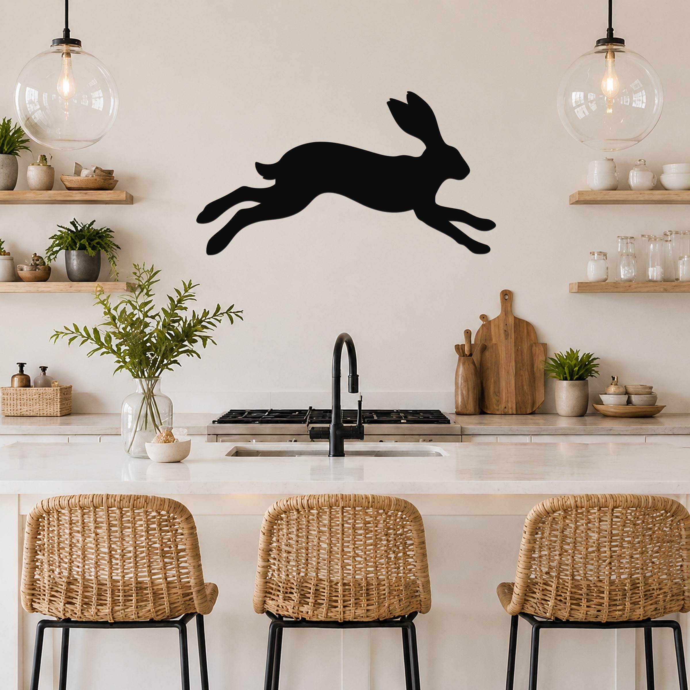 Black metal jackrabbit wall art silhouette mounted above a kitchen counter, displayed in a modern kitchen with open shelving and pendant lights.