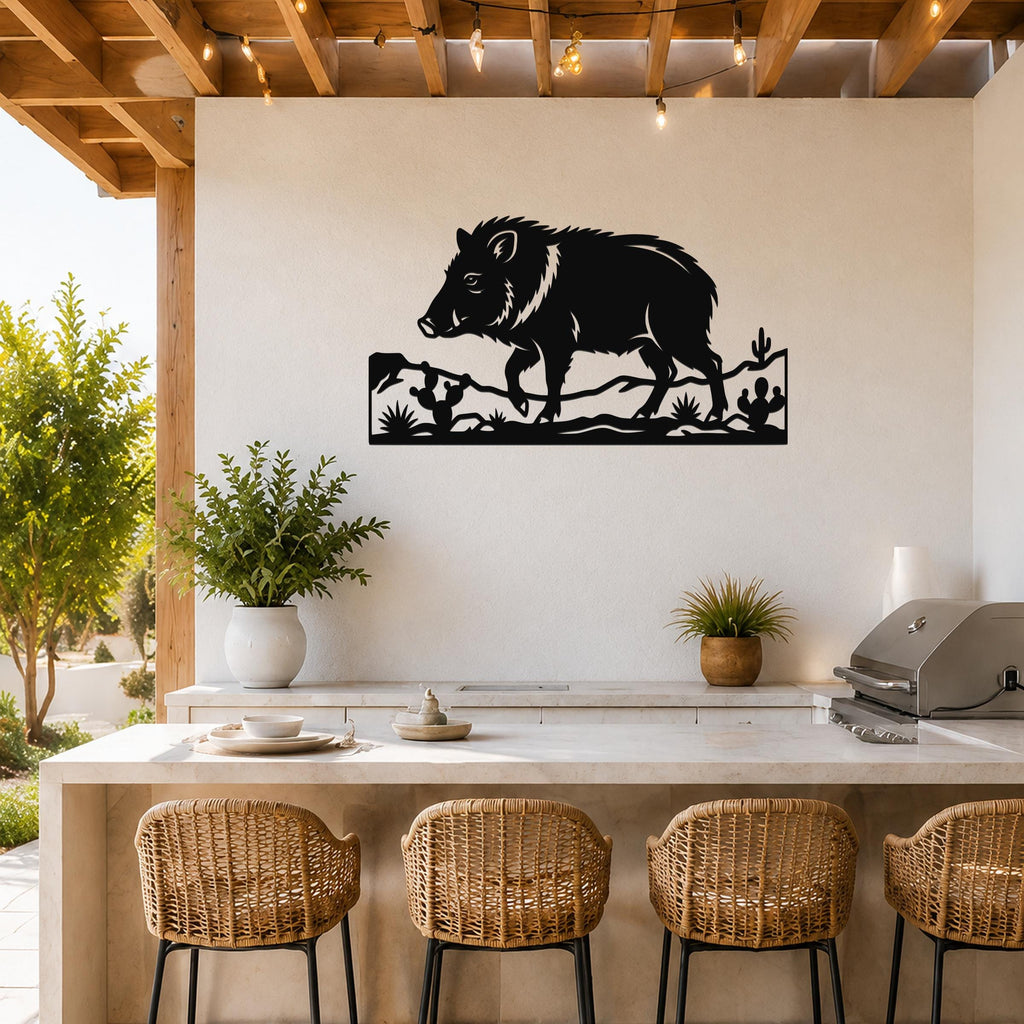 Black metal javelina wall art with cactus and terrain cutouts, mounted on a white wall above a kitchen counter in a covered patio.
