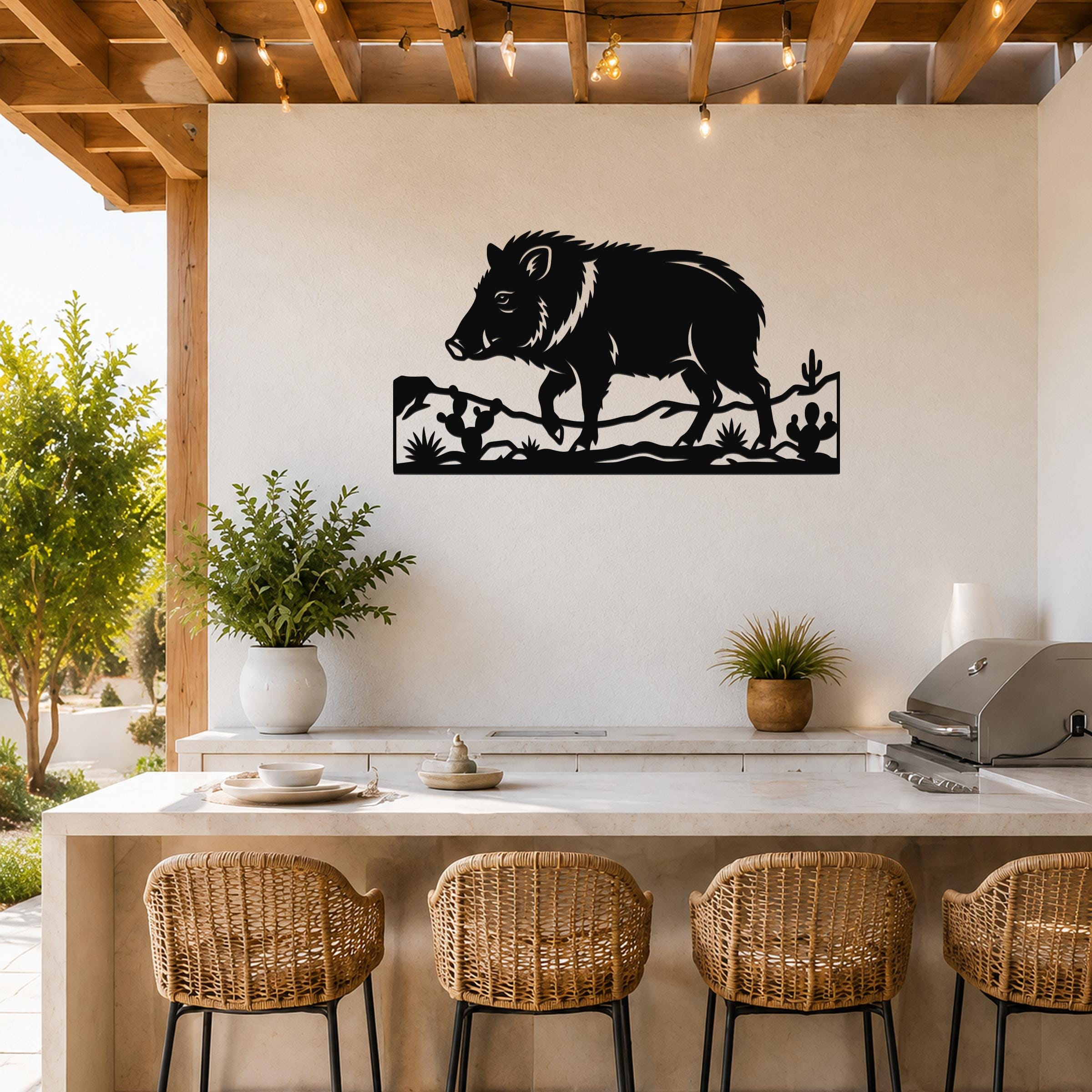 Black metal javelina wall art with cactus and terrain cutouts, mounted on a white wall above a kitchen counter in a covered patio.