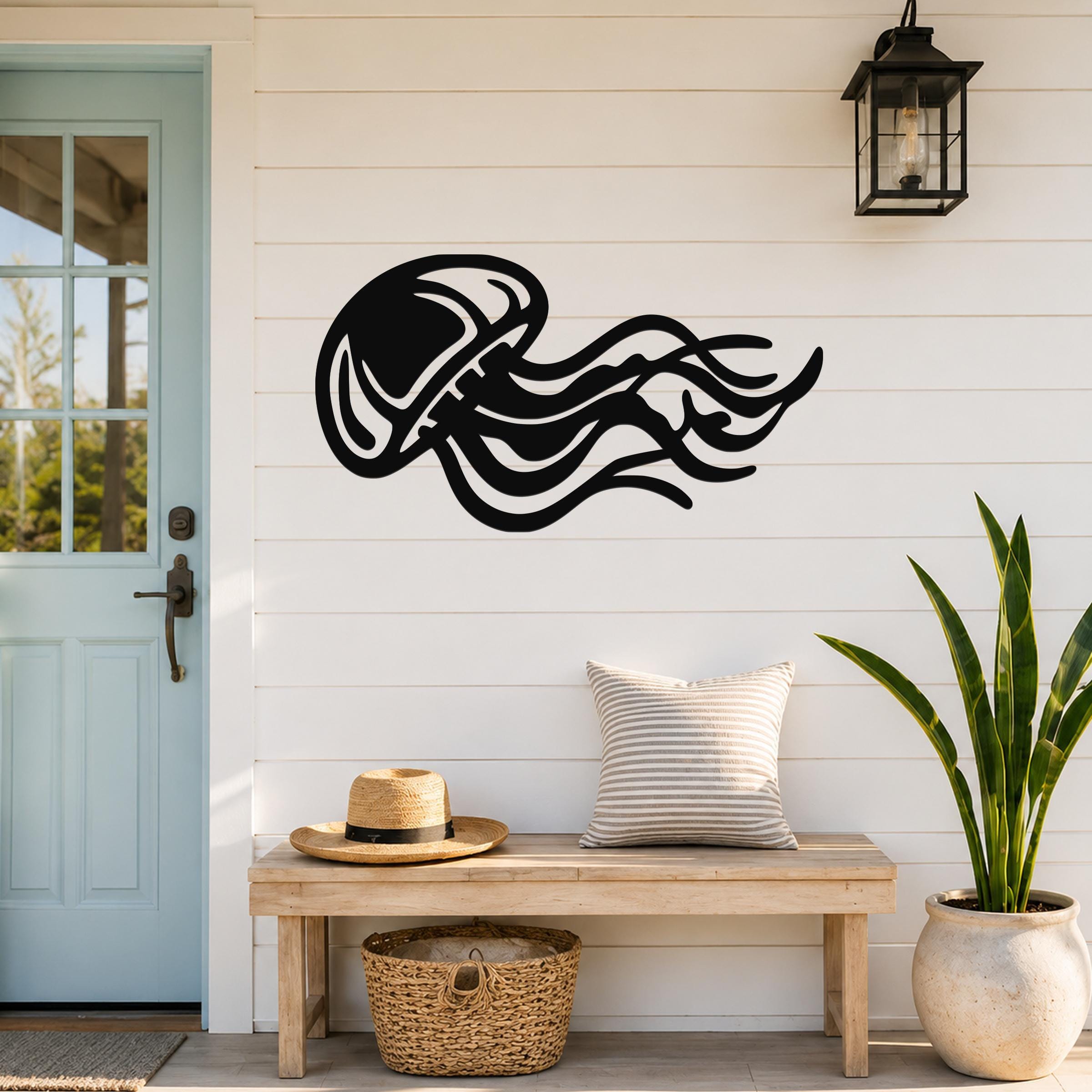 Black metal jellyfish wall art with flowing tentacle cutouts, mounted on a white shiplap wall above a wooden bench in a coastal entryway.