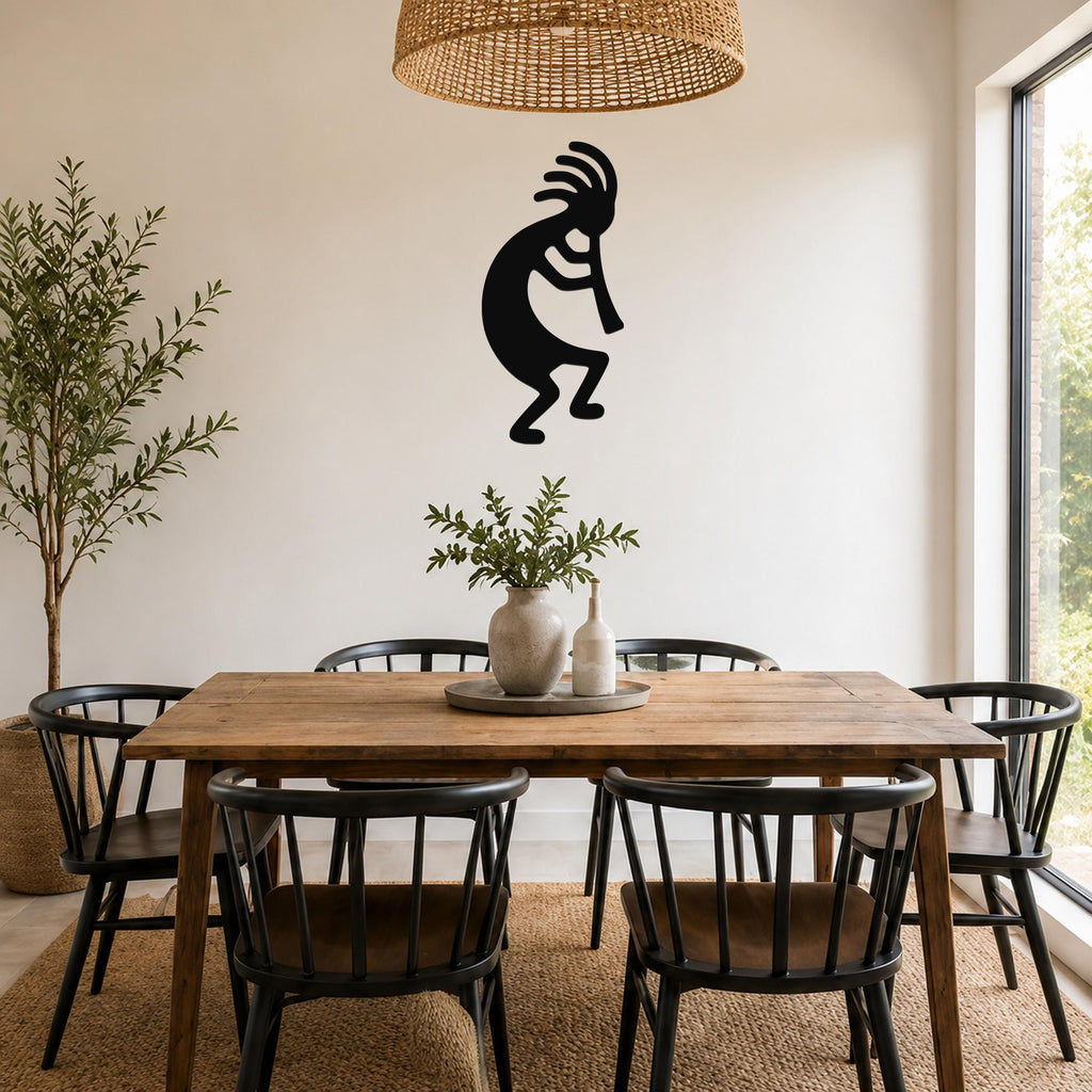 Black metal Kokopelli wall art silhouette with flute and feathered headdress, mounted on a dining room wall above a wooden table.
