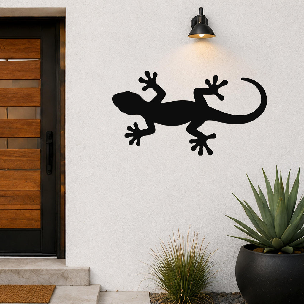 Black metal gecko wall art silhouette mounted on a white exterior wall beside a wooden door and potted plants.