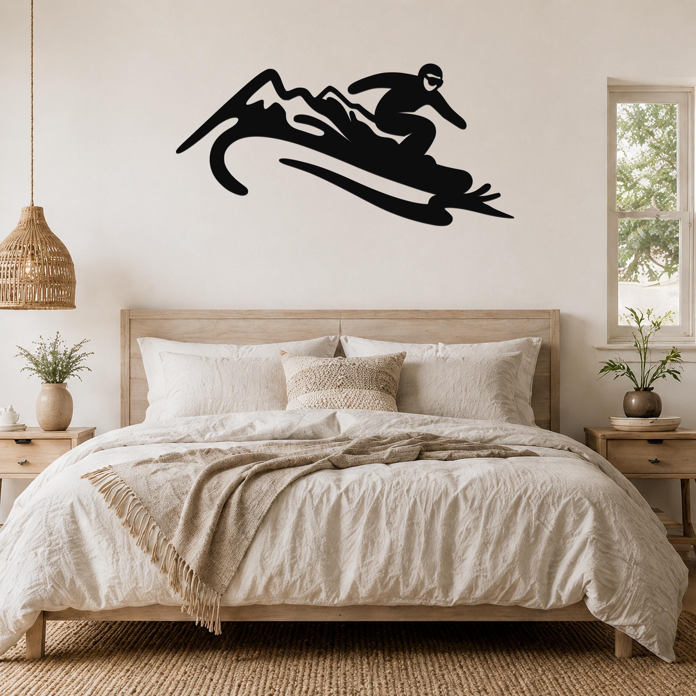 Black metal wall art silhouette of a snowboarder in motion, mounted above a bed in a bedroom.