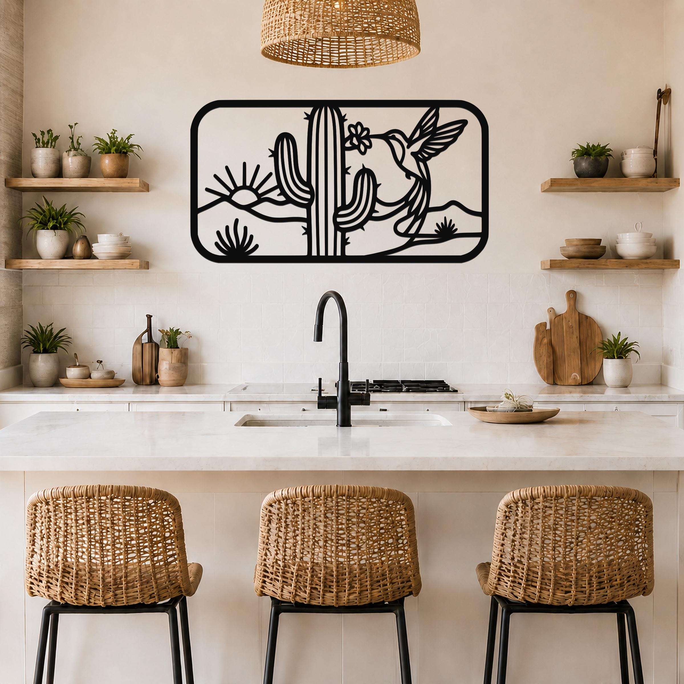 Black metal wall art with a desert scene silhouette featuring a saguaro cactus, hummingbird, and sun, mounted above a kitchen counter.
