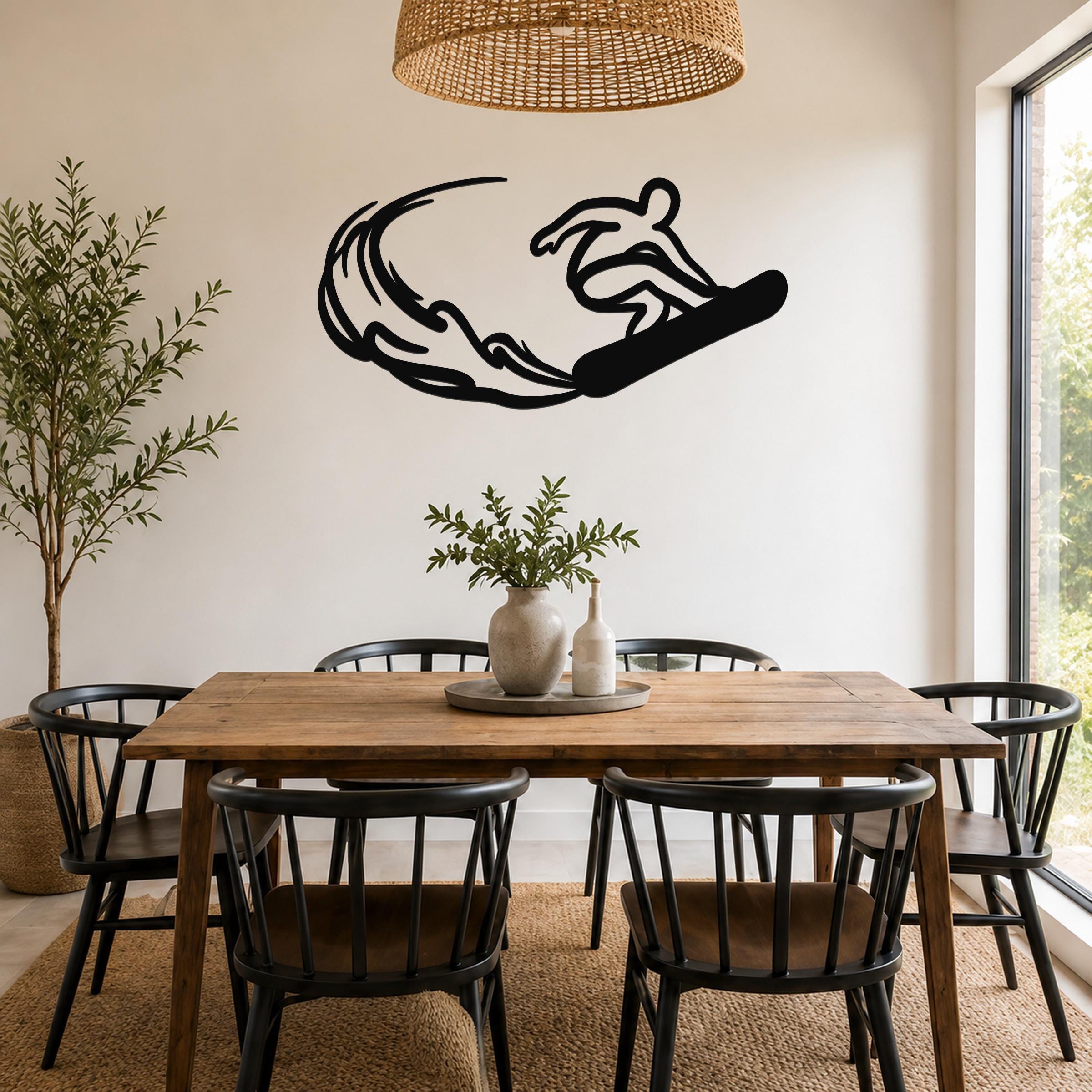 Black metal wall art silhouette of a snowboarder in motion, mounted above a wooden dining table in a bright room.