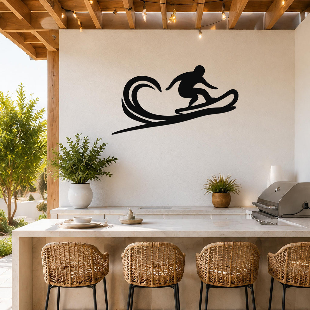 Black metal wall art silhouette of a surfer on a wave, mounted above a kitchen counter on a white outdoor patio wall.