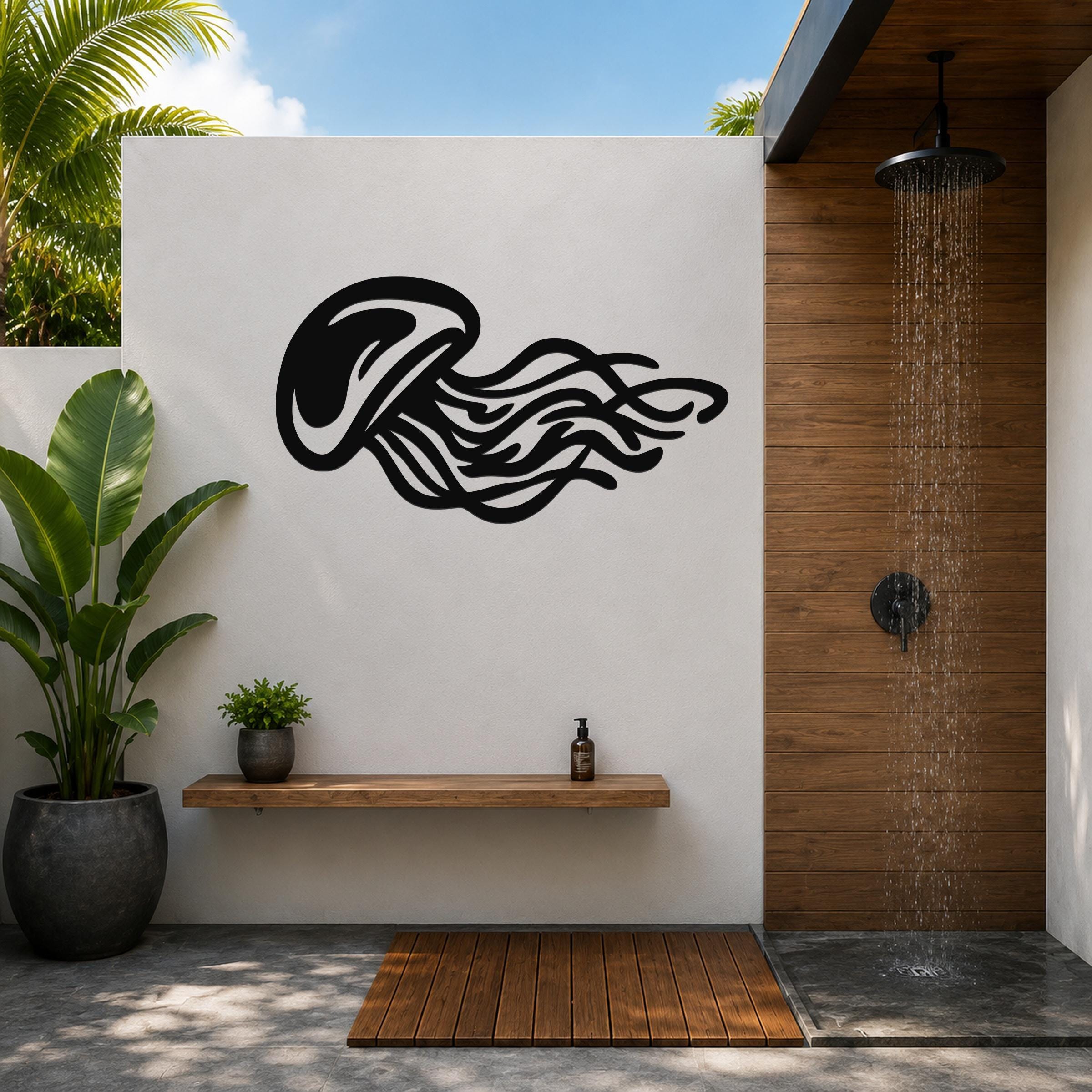 Black metal jellyfish wall art with flowing tentacle cutouts, mounted on a white outdoor wall above a wooden shelf in a tropical shower area.