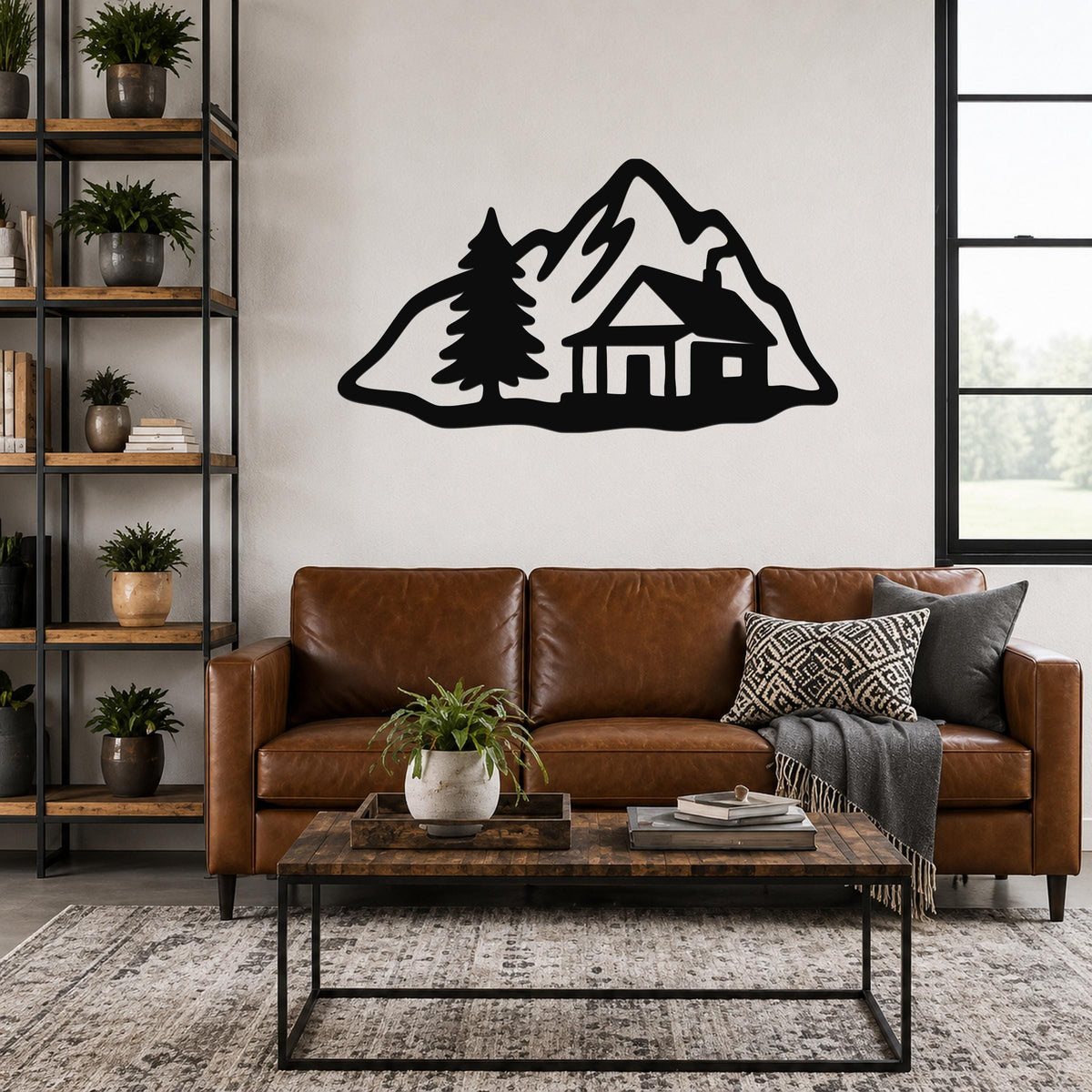 Black metal wall art silhouette of a mountain cabin with a pine tree, mounted above a brown leather sofa in a living room.