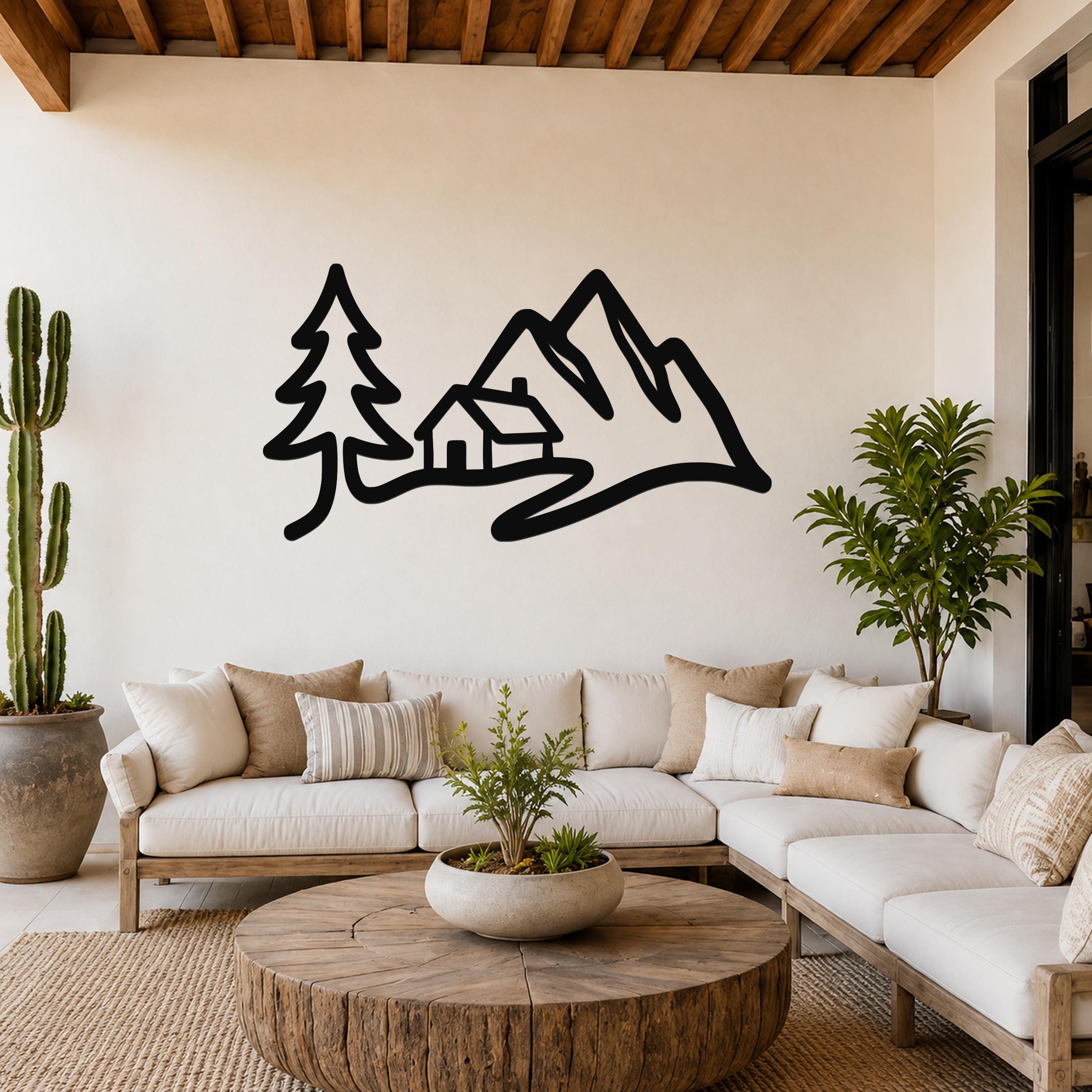 Black metal wall art silhouette of a mountain range, cabin, and pine tree, mounted above a white sofa in a living room.