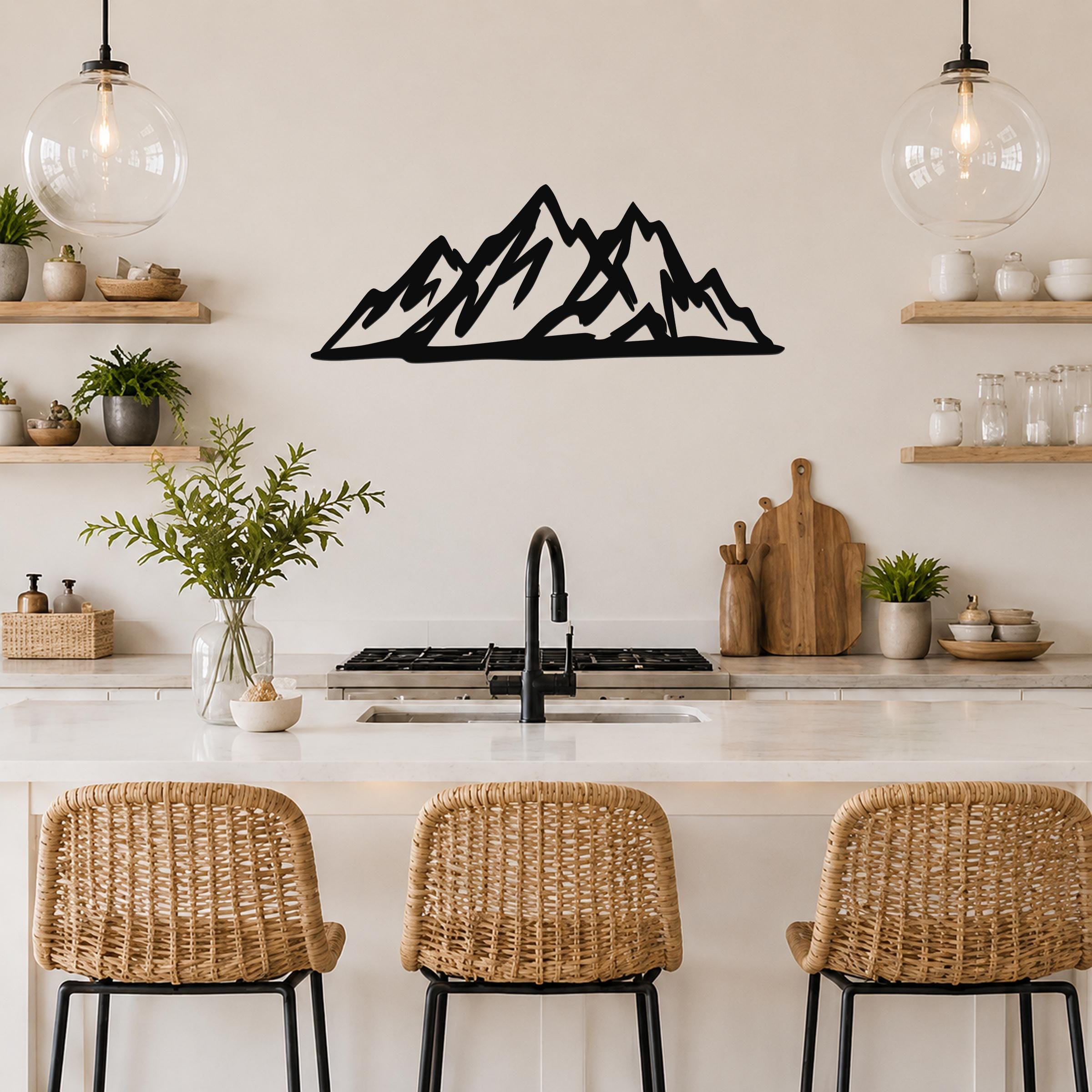 Black metal mountain silhouette wall art with layered peaks, mounted on a kitchen wall above a counter with wicker bar stools.